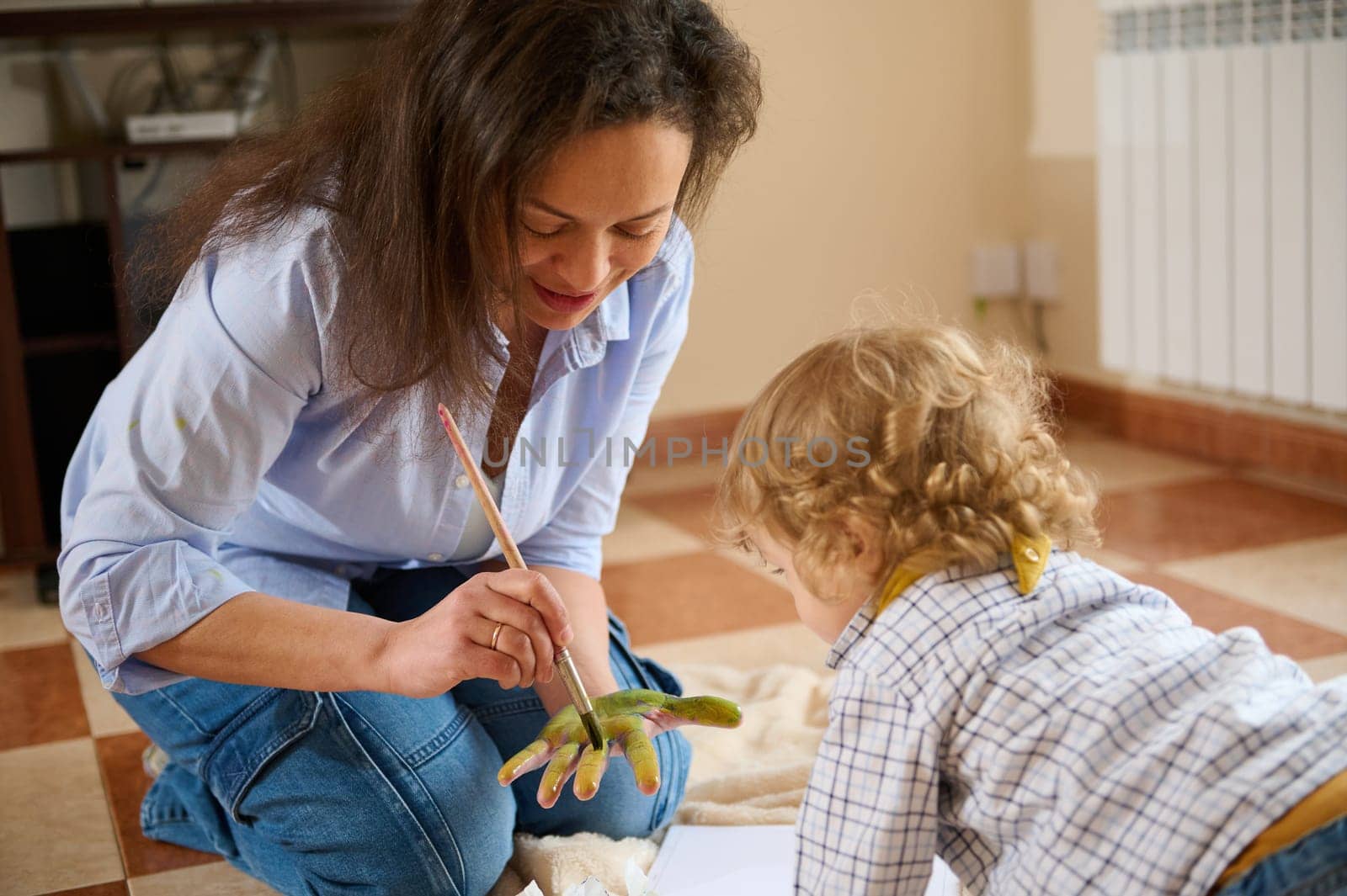 A loving moment of a mother painting her child's hand, emphasizing the bond and creativity shared in a cozy home setting.
