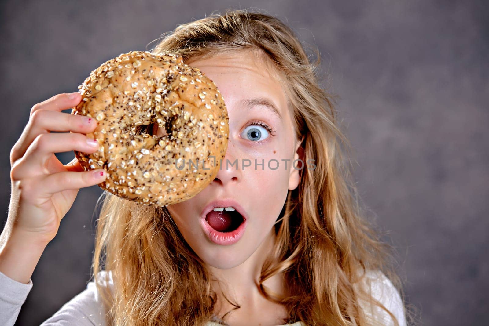 nice blond girl in front of gray background looking through a big bagel