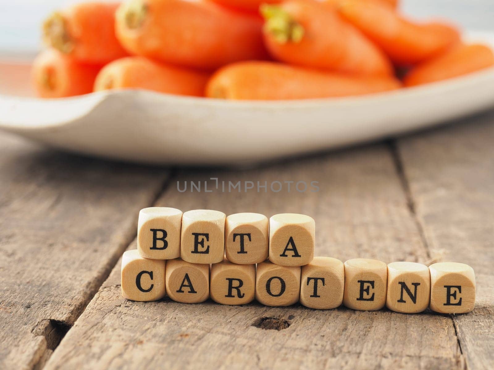 Wooden dices with the words beta carotene and fresh carrots in the back, healthy eating concept