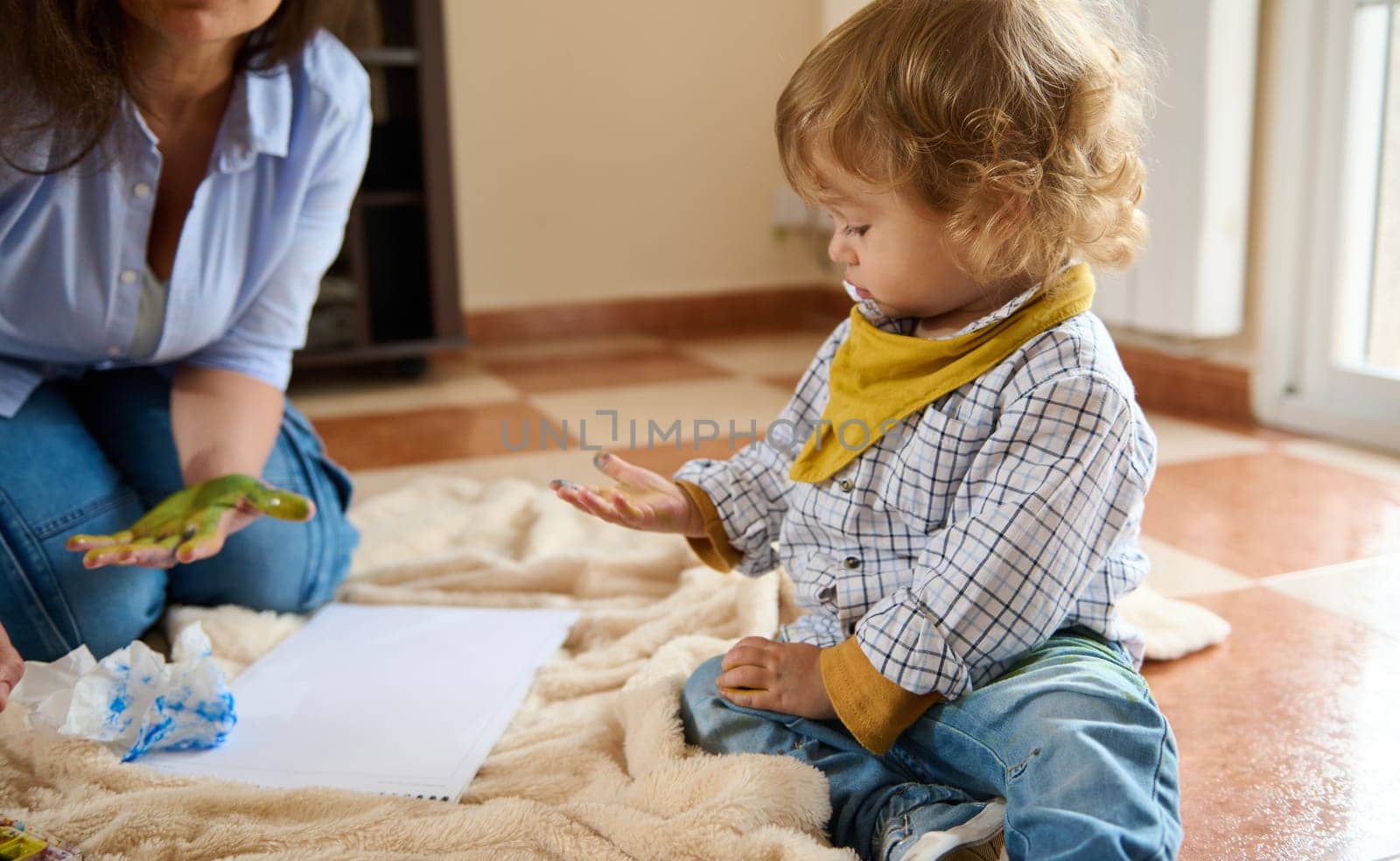 Young child and caregiver engaging in hands-on painting activity indoors, enjoying a creative bonding moment together and fostering imagination and emotional connection in a warm, cozy environment.