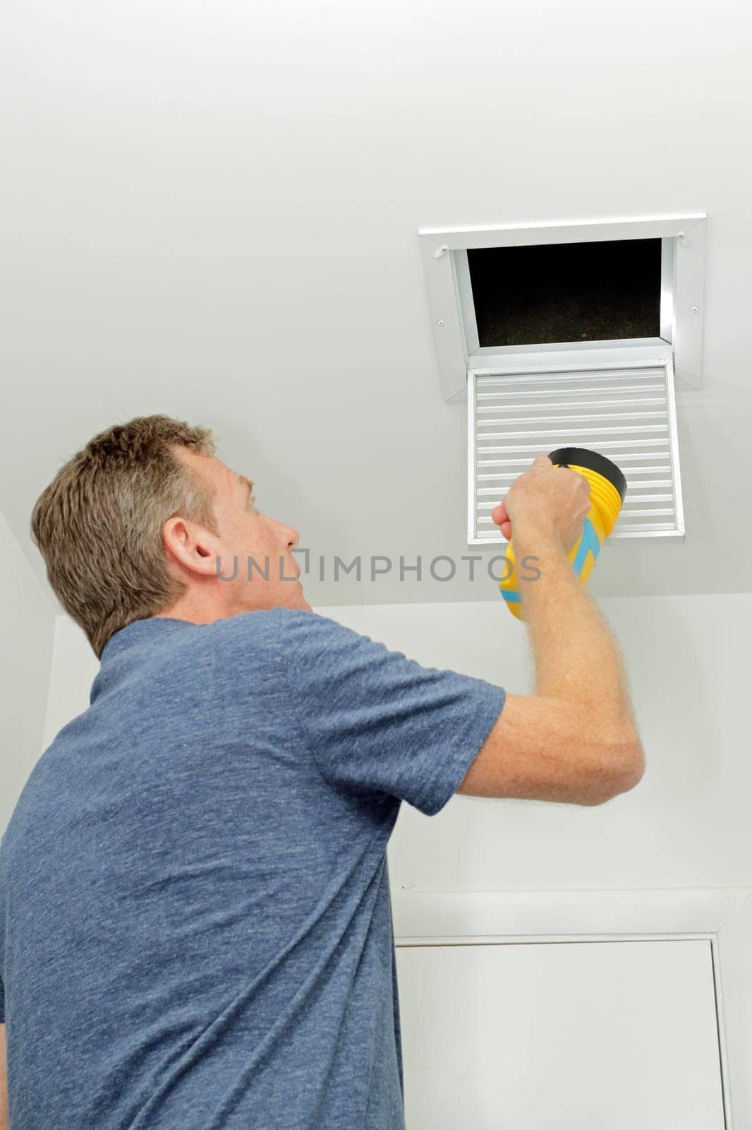 Homeowner looking into a small air duct searching for and dirt and examining the condition. Male examining the cleanliness of a small home HVAC air duct..