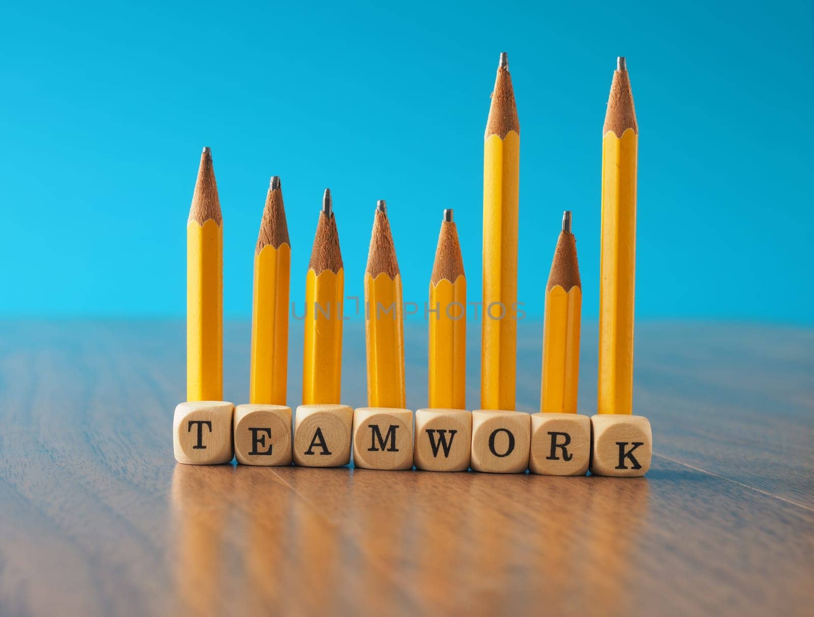 Teamwork concept with a row of yellow pencils and wooden dices with the word teamwork on an office table