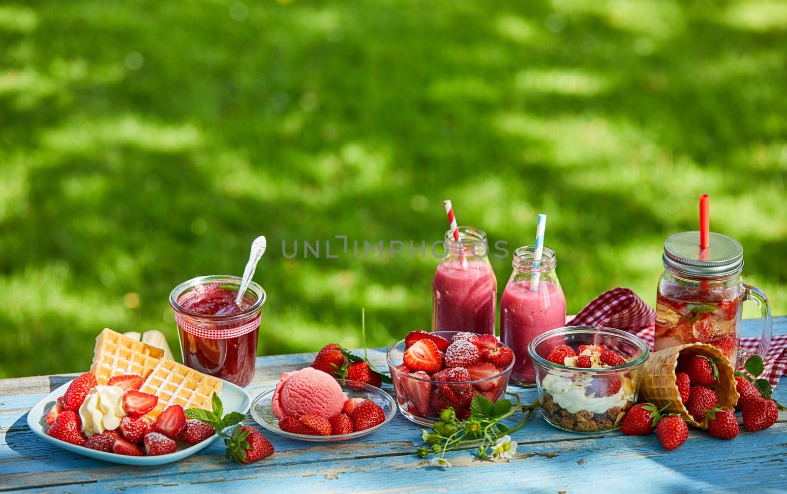 Fresh, healthy, vibrant summer strawberry smoothie bowl, juices and desserts picnic on a bright outdoor table setting.