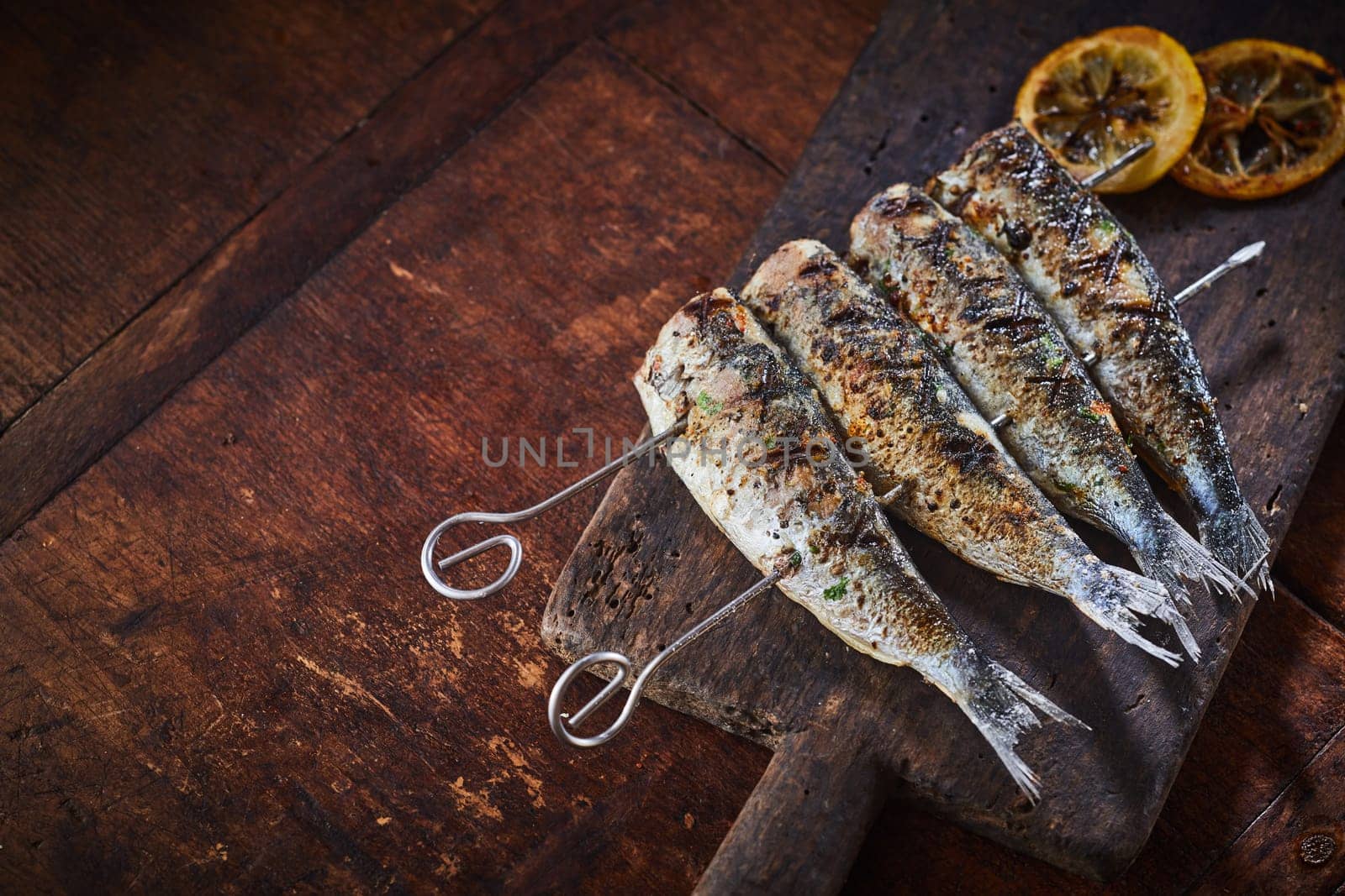 Grilled fish on skewers served on rustic wooden table viewed in close-up from above with copy space