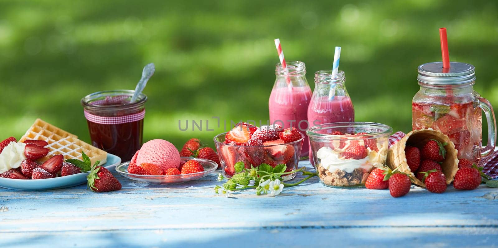 Fresh, healthy, vibrant summer strawberry smoothie bowl, juices and desserts picnic on a bright outdoor table setting.