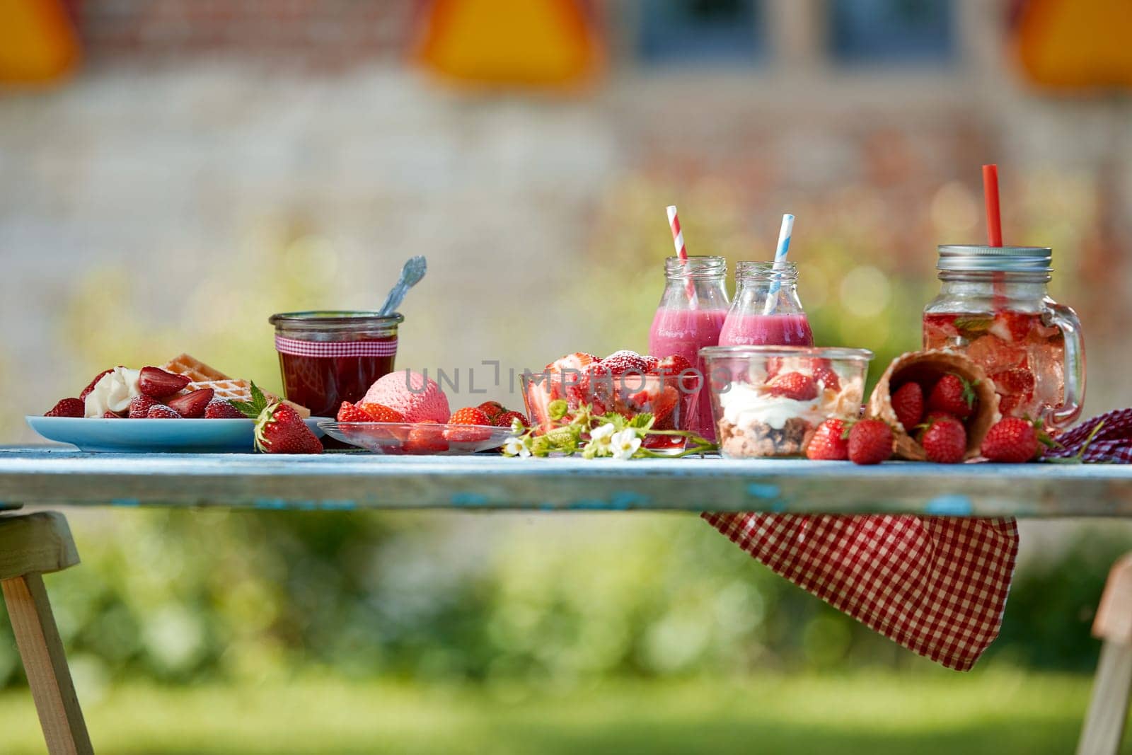 Fresh, healthy, colourful summer strawberries smoothie bowl, juices and desserts picnic on a bright outdoor table setting.