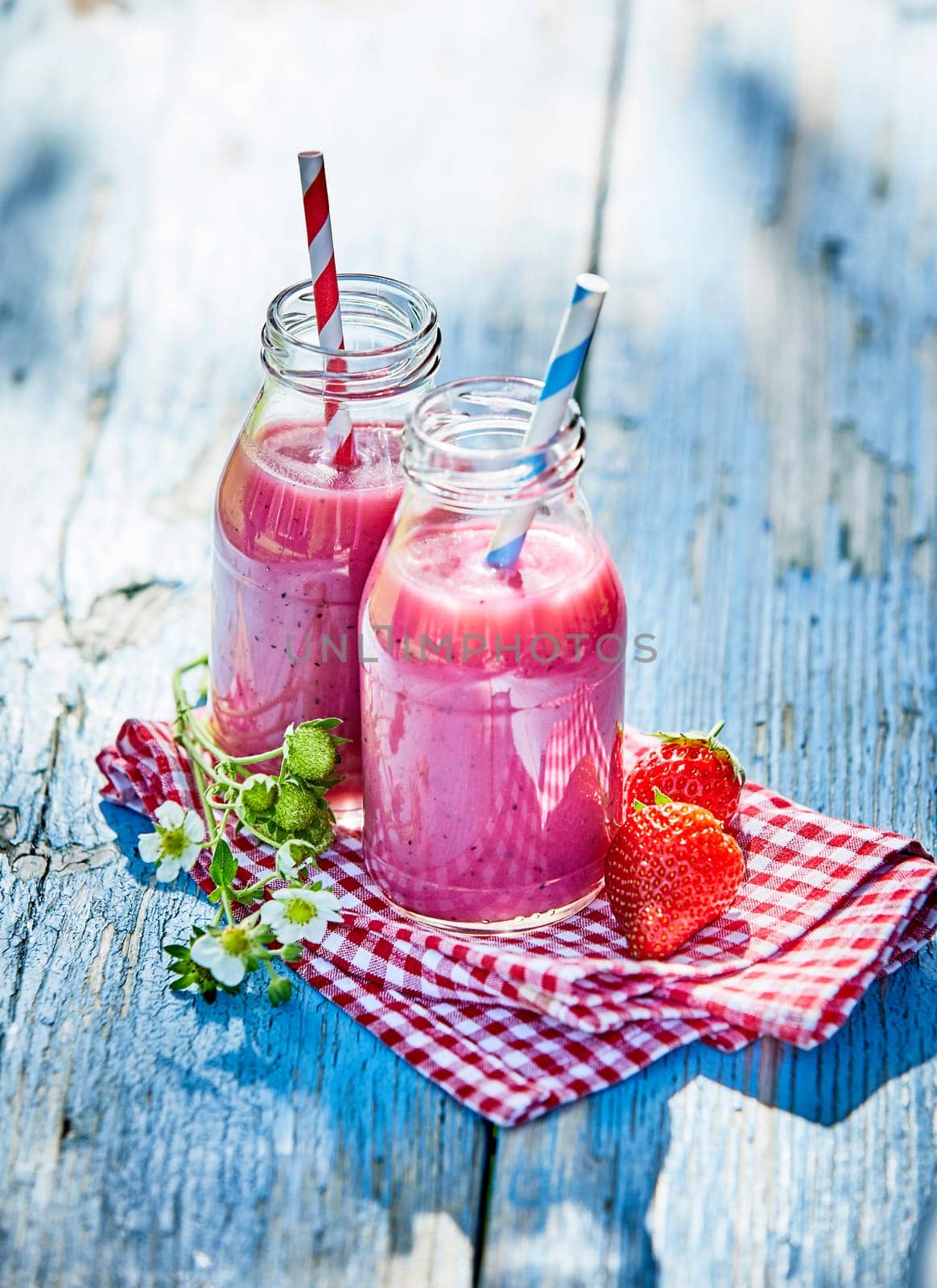 Vibrant strawberry smoothies in glass jars on an outdoor summer picnic table setting.