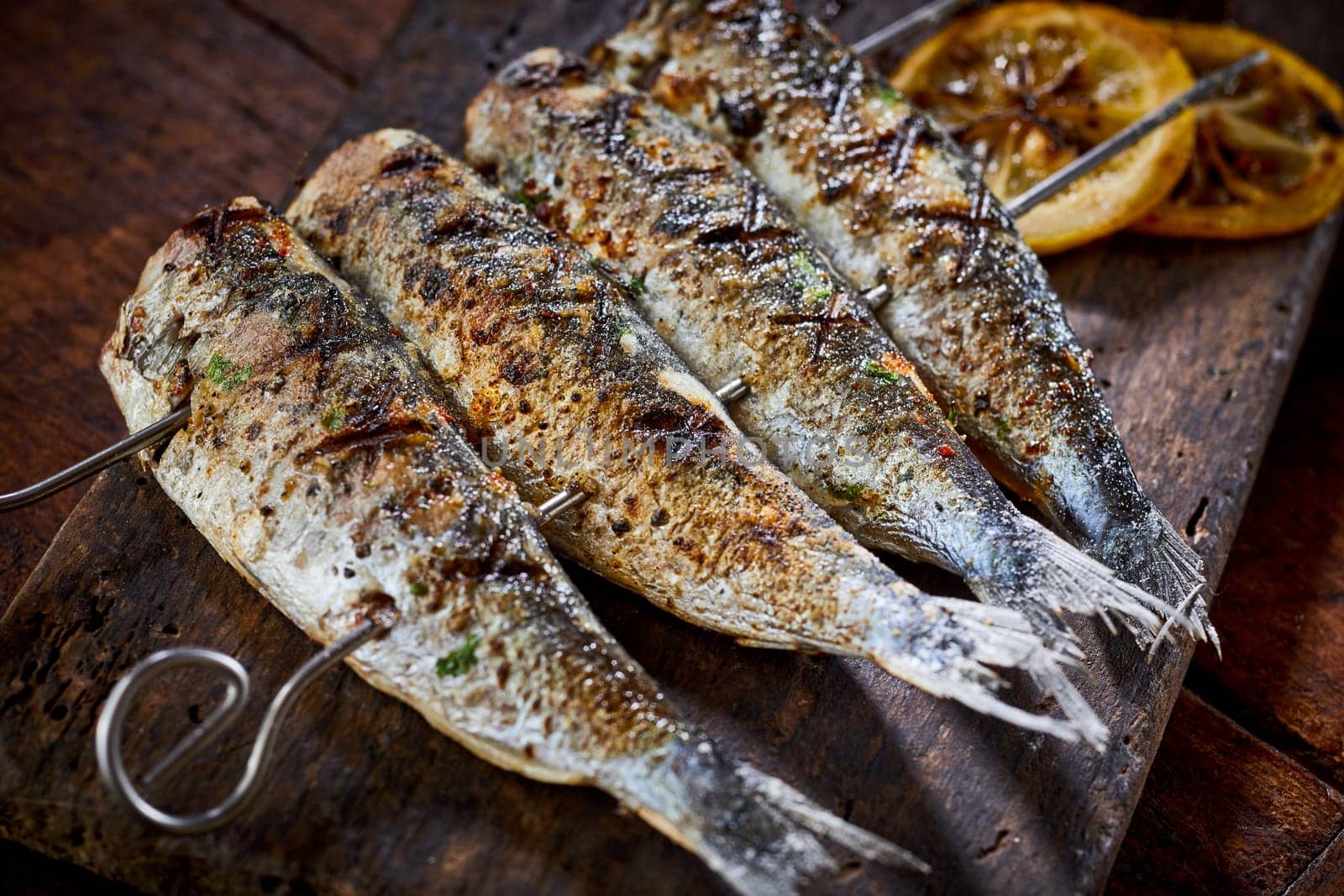 Four spicy grilled fresh fish on skewers on an old rustic wooden board from a summer barbecue