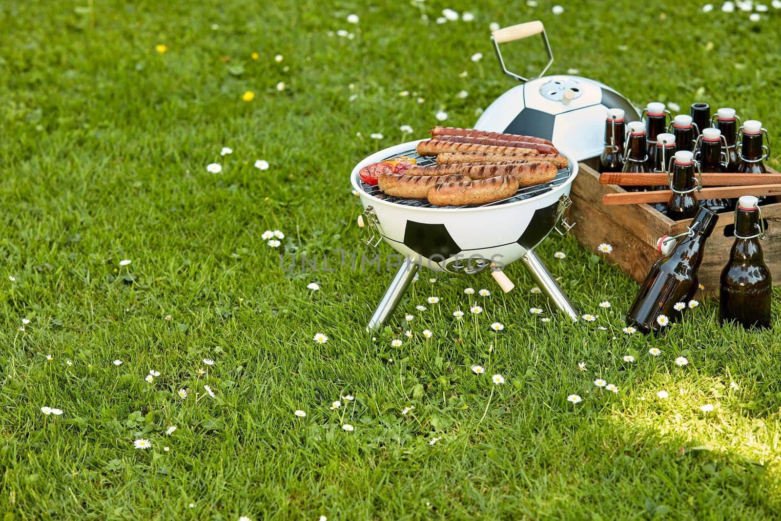 Celebration barbecue for the World Cup Soccer with sausages grilling over a ball shaped portable BBQ with a crate full of bottled beer alongside in a meadow