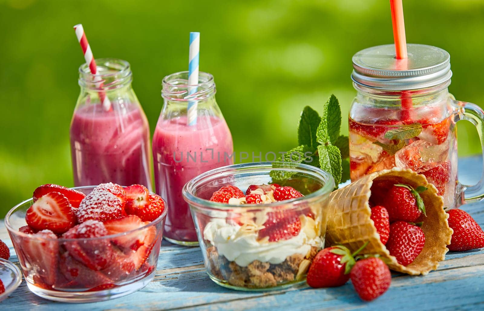 Fresh, sweet, healthy summer berry smoothie bowls and juices on a bright outdoor table setting.