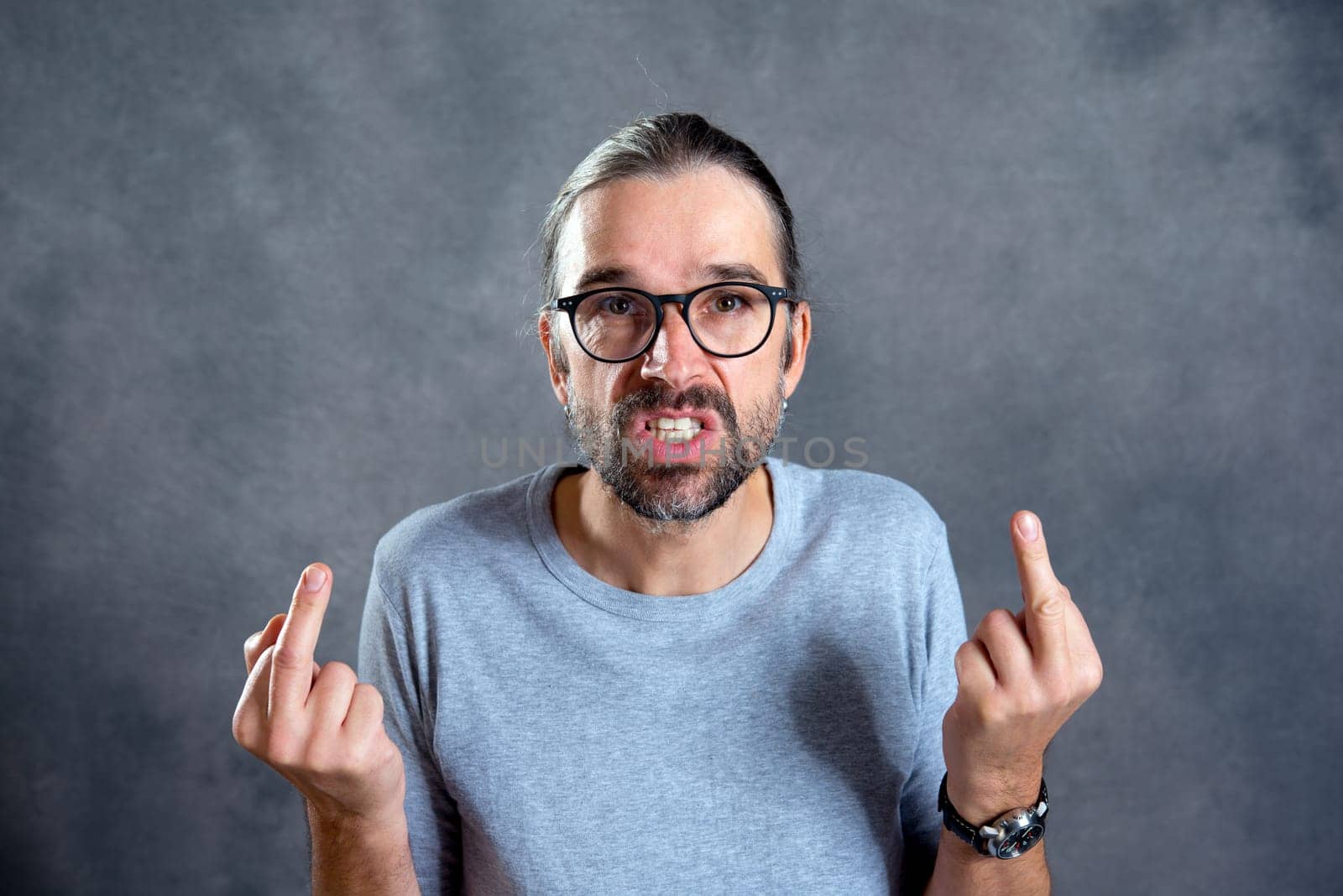 young man in front of gray background showing middle finger