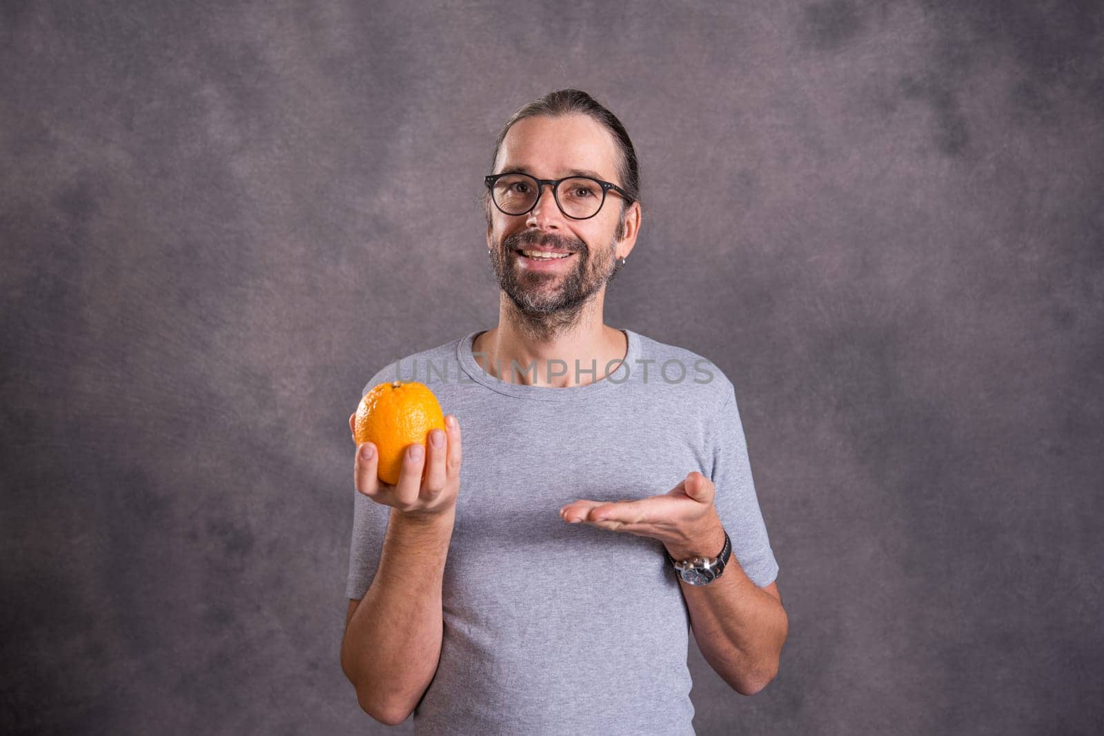 long haired young man with orange in front of gray background