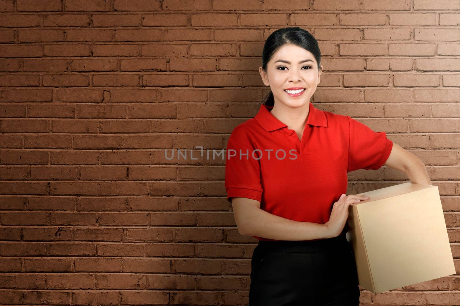 Pretty asian courier woman bring the package with wall background