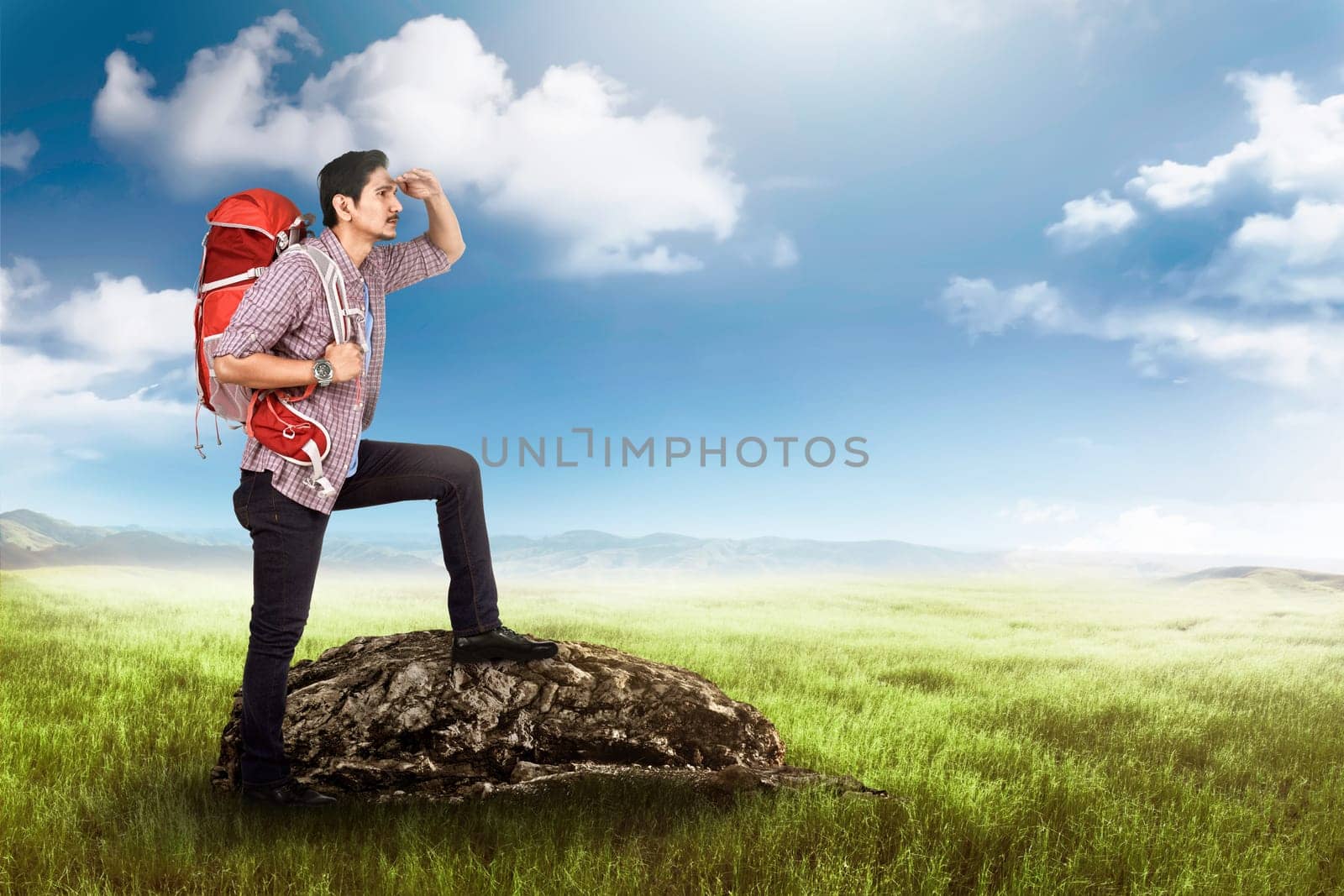 Handsome asian tourist with backpack standing on the stone at meadow field