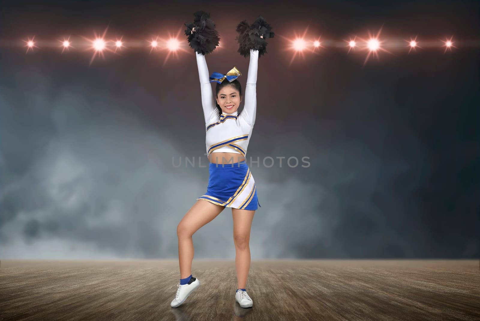 Smiling asian cheerleader perform with pom-poms with spotlights on background