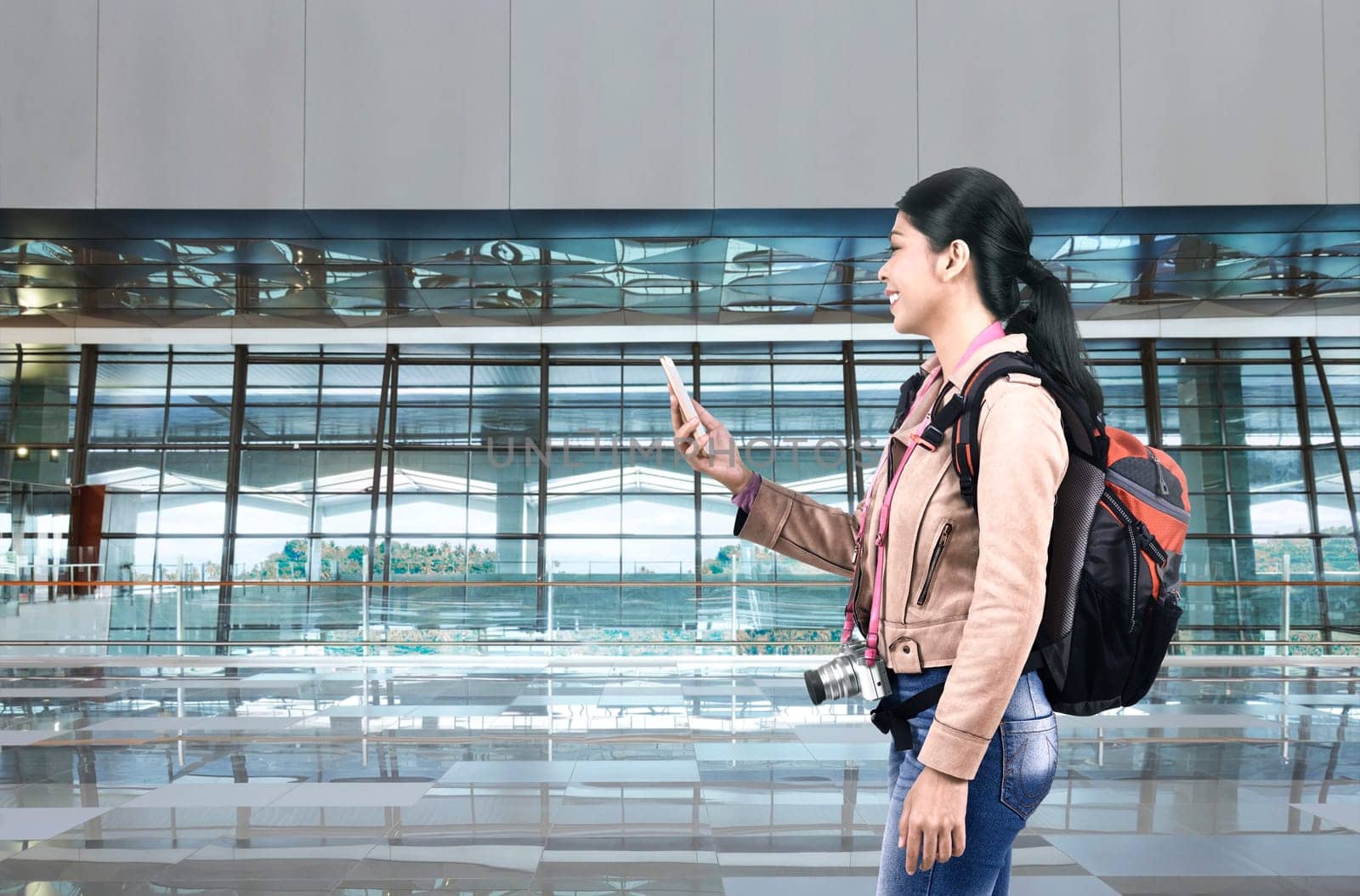 Smiling asian tourist woman with backpack using cellphone on the airport