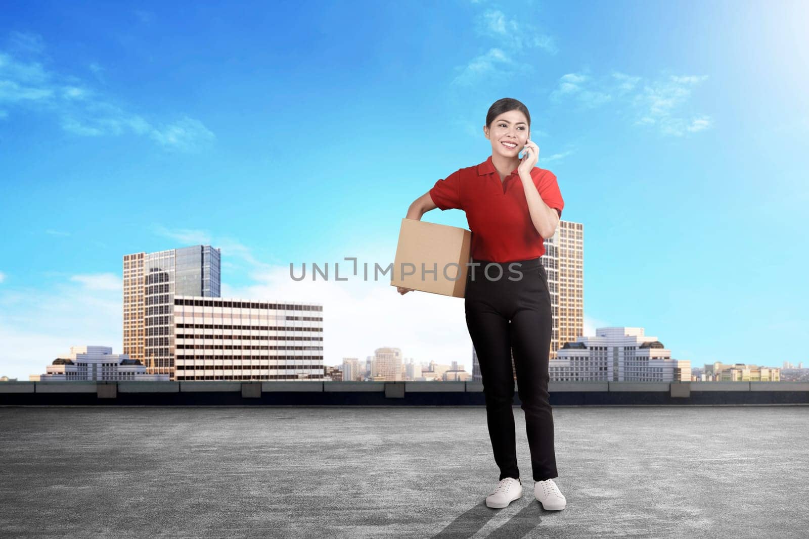 Young asian delivery woman with package talking on the cellphone on the city