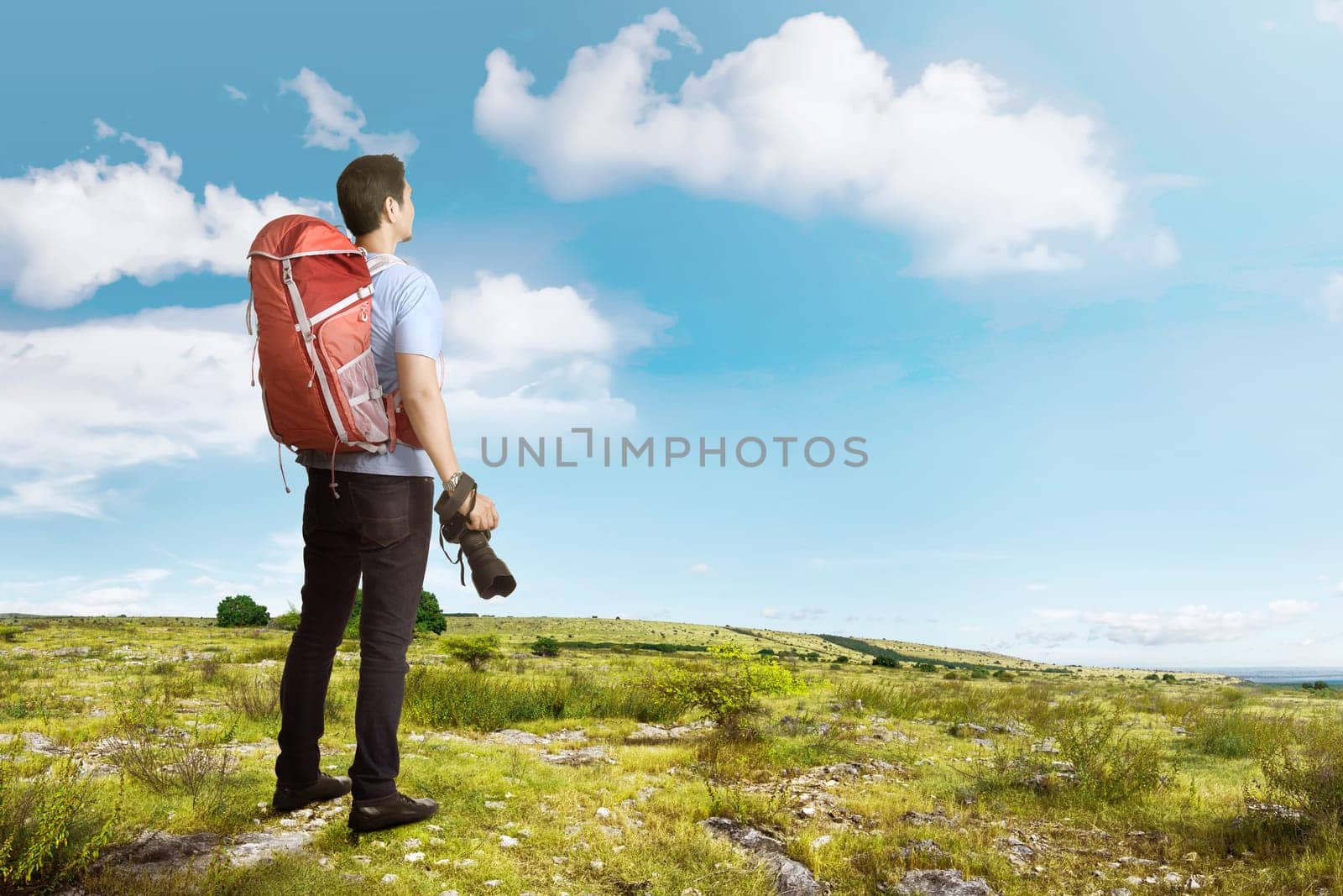 Attractive asian traveler man with backpack and camera on the meadow