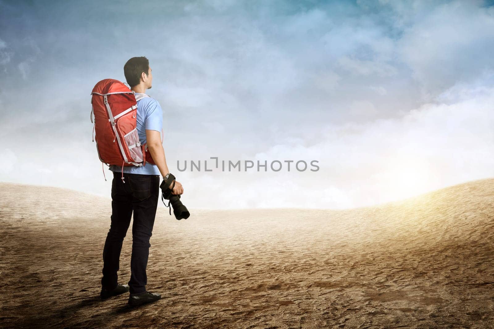 Back view of asian backpacker man holding camera on the mountain