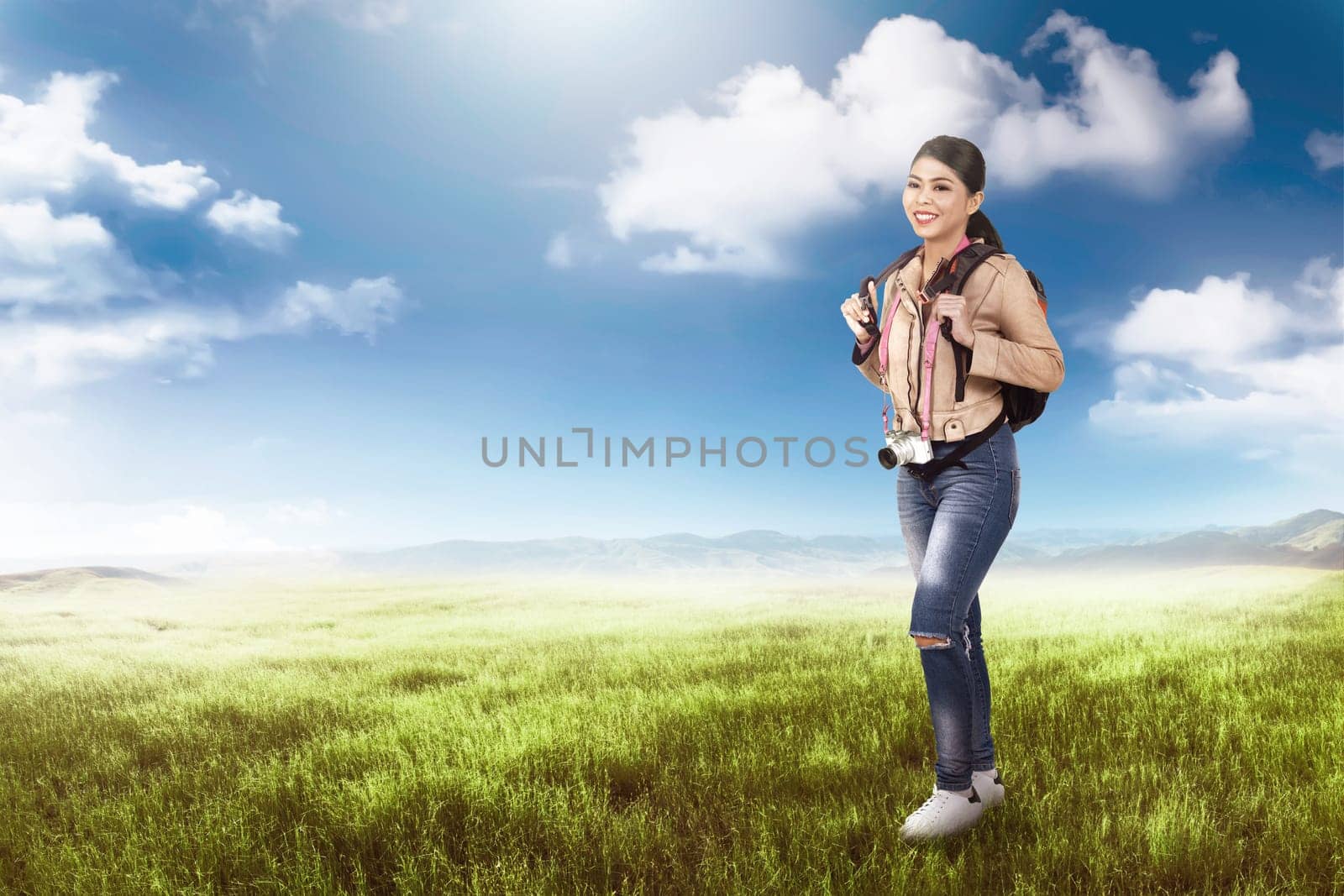 Beautiful asian traveler woman with camera and backpack relaxing on the meadow