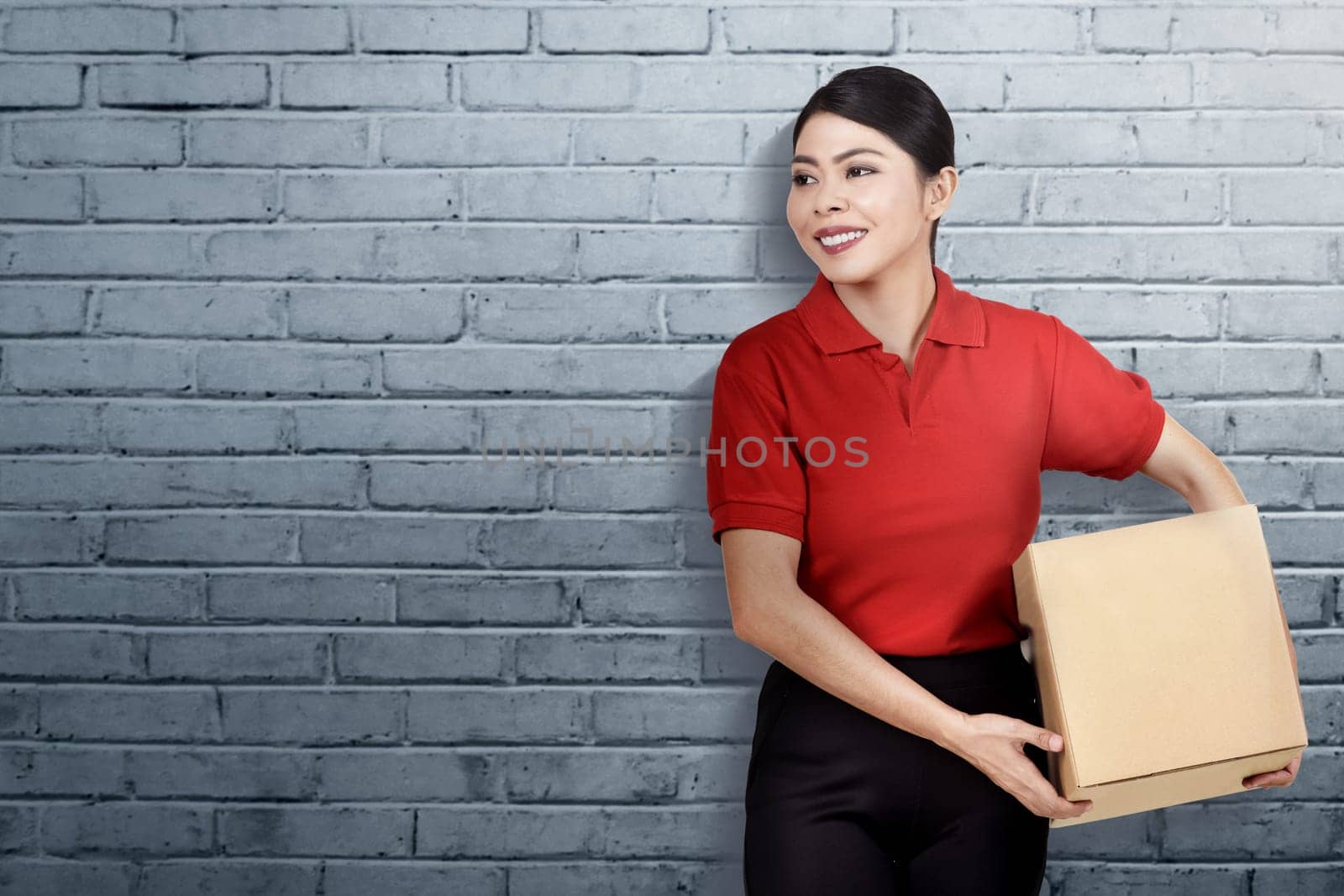 Smiling asian delivery woman carrying the parcel with wall background