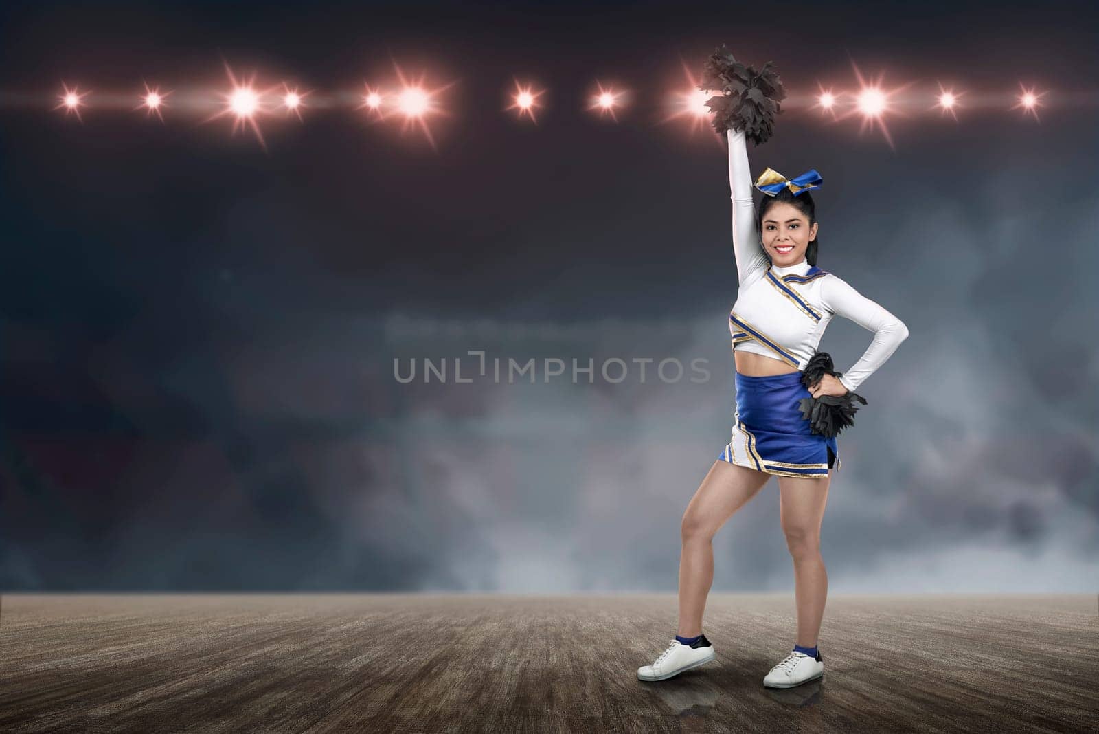 Attractive asian cheerleader holding pom-poms with spotlights on background