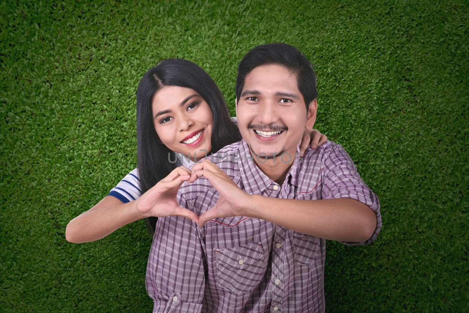 Happy asian couple in love make a heart shape with hands over green background