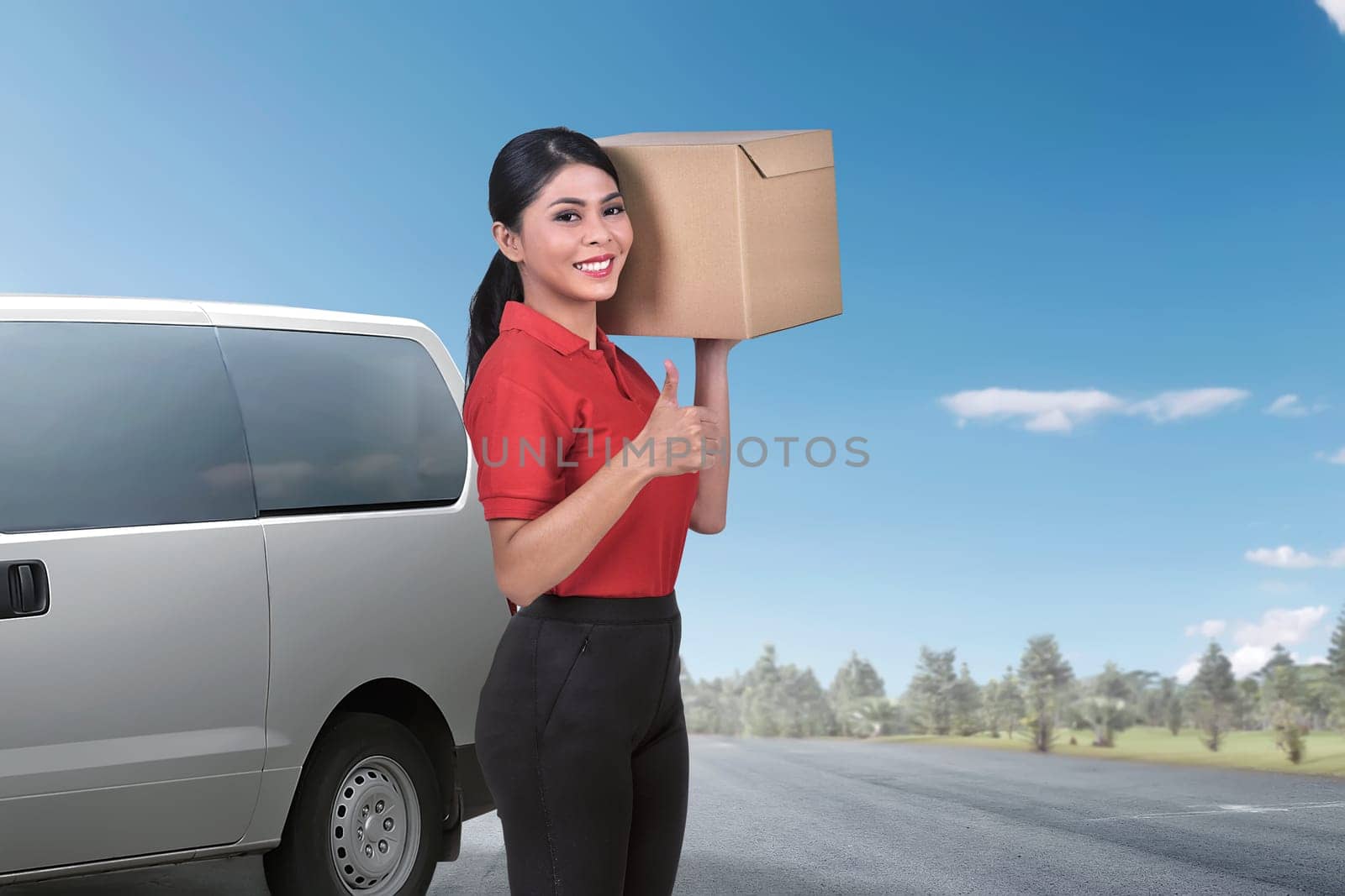Pretty asian delivery woman standing with the package against van on the background