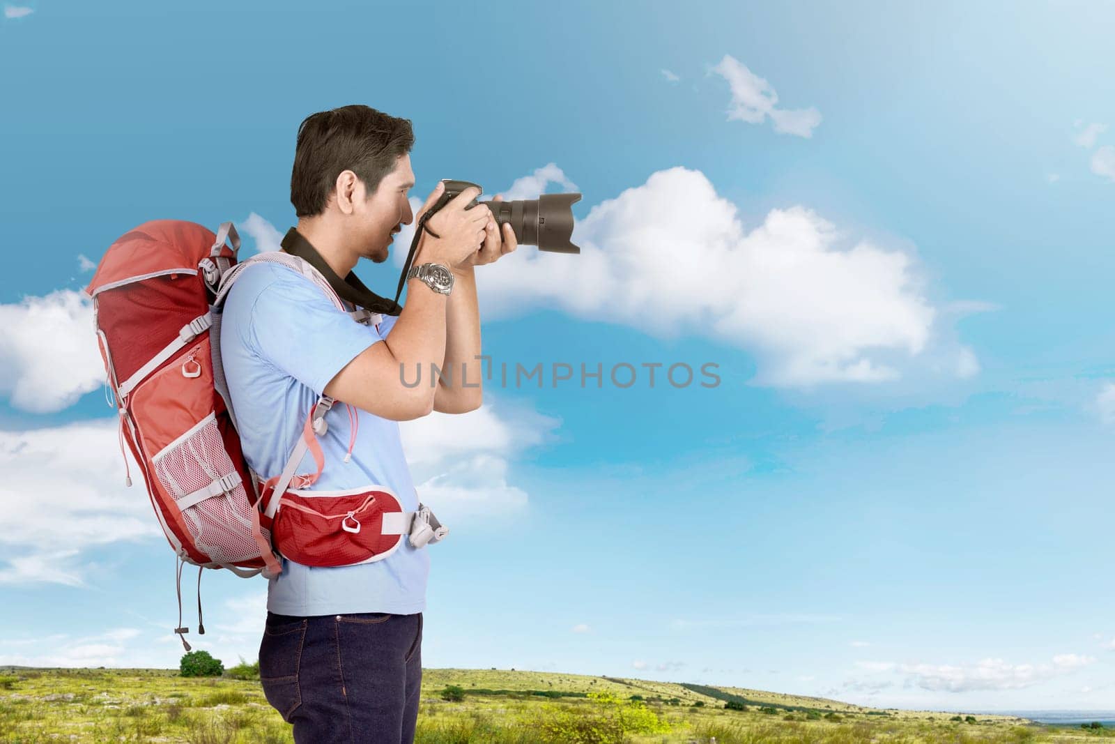 Side view of asian photographer man with backpack on the meadow field
