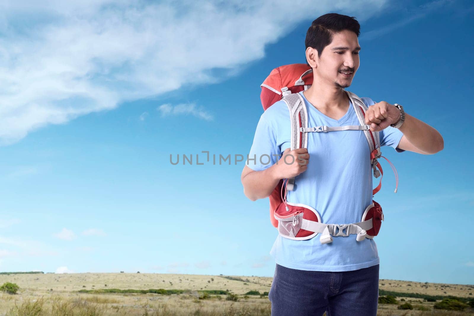 Cheerful asian traveler with backpack checking the time at day