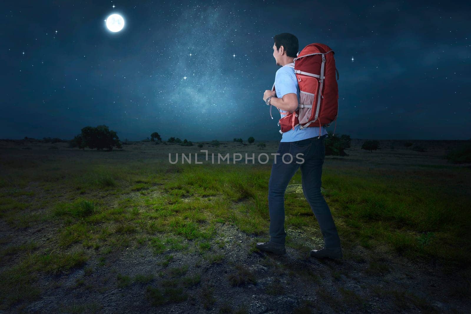 Attractive asian traveler with backpack walking on the field at night