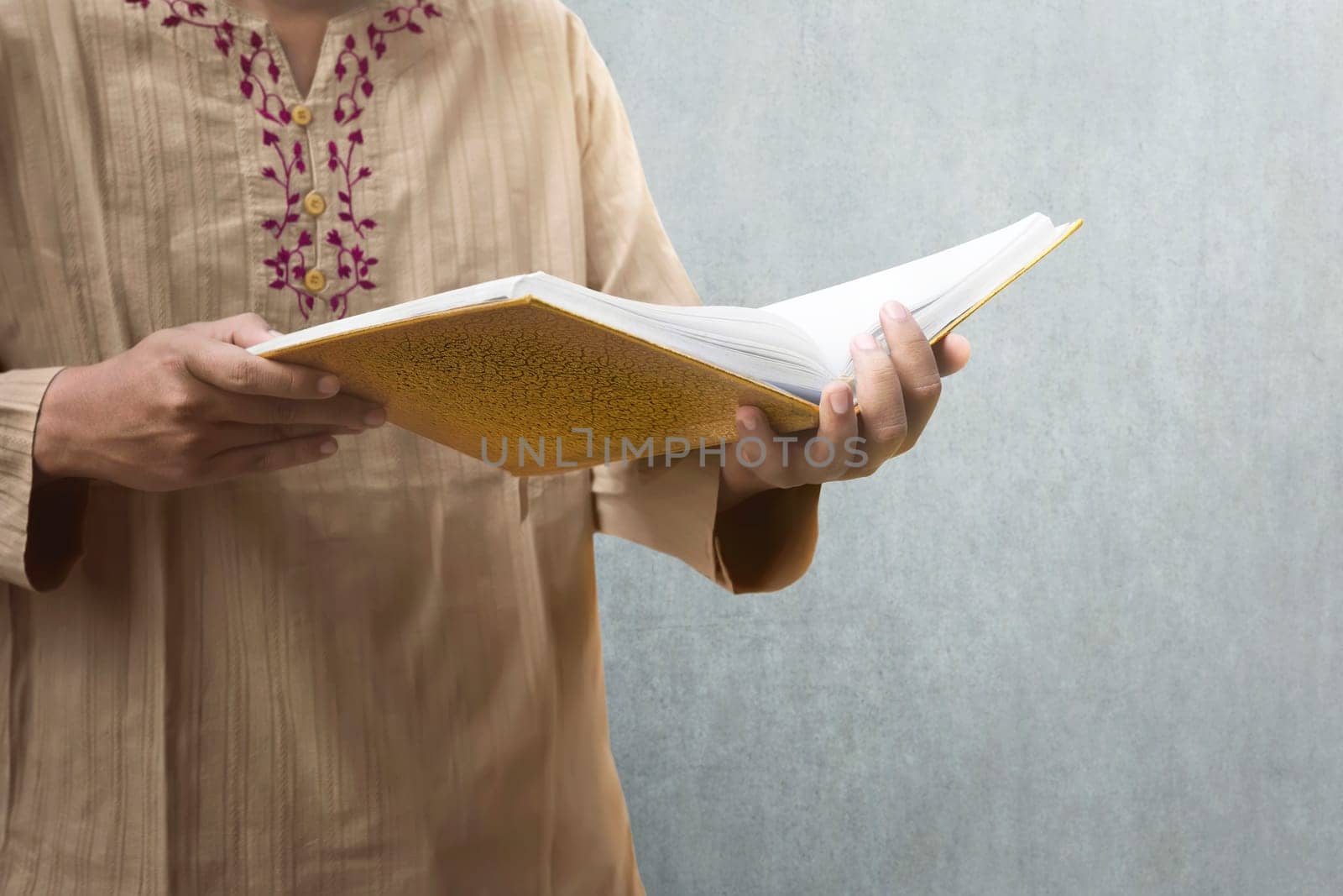 Muslim man reading the Koran with wall background