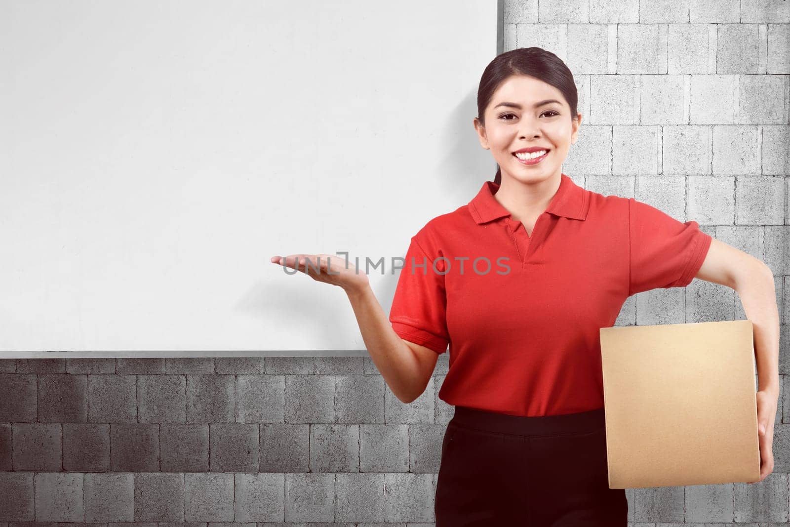 Young asian delivery woman carrying parcel and showing copyspace with whiteboard background
