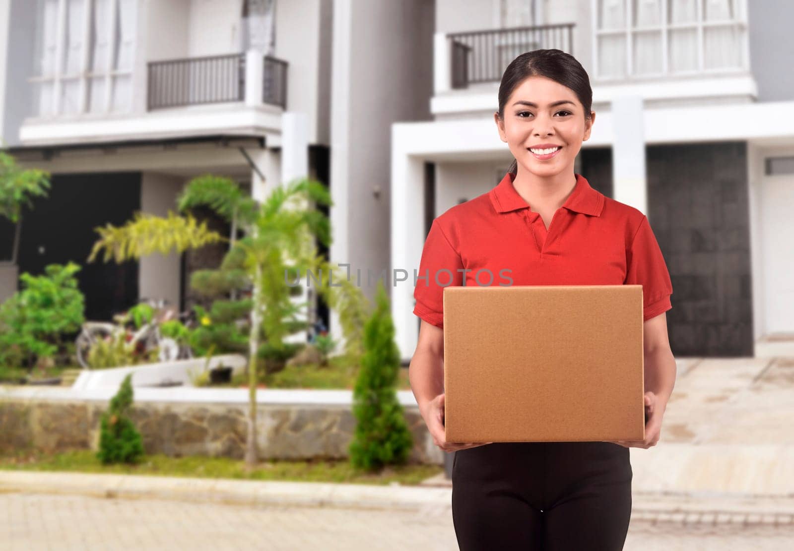 Young asian courier woman delivering package in front of house of packet receiver