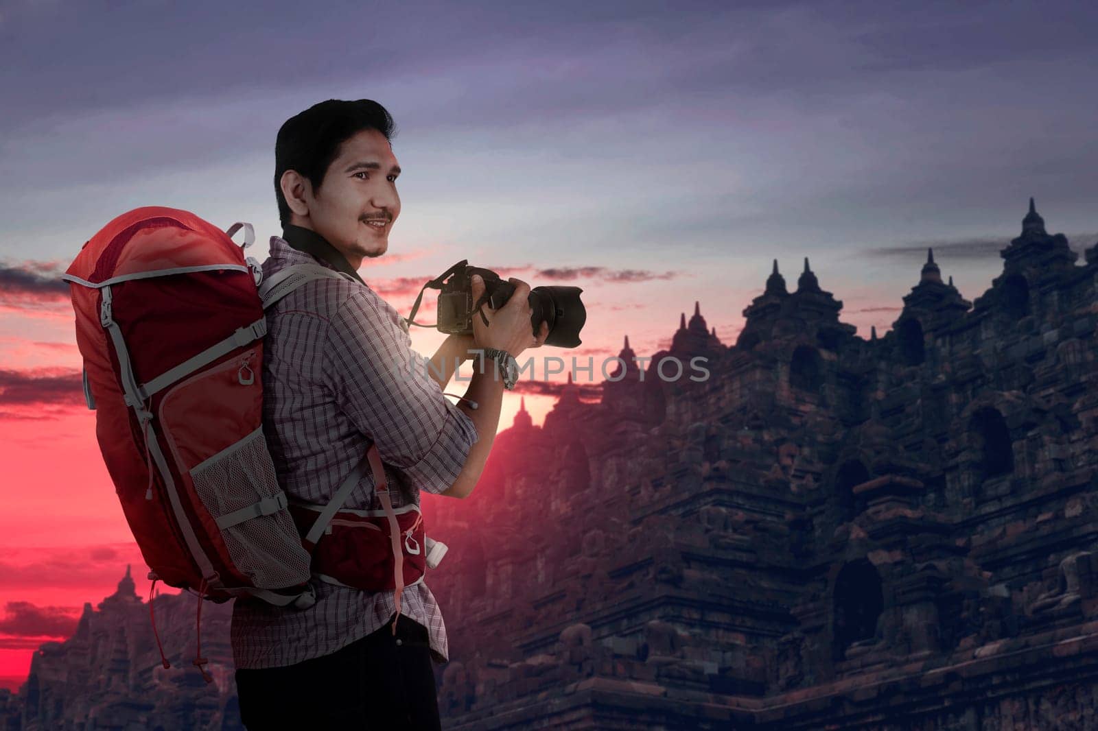 Smiling asian traveler with backpack and camera taking photos at sunset