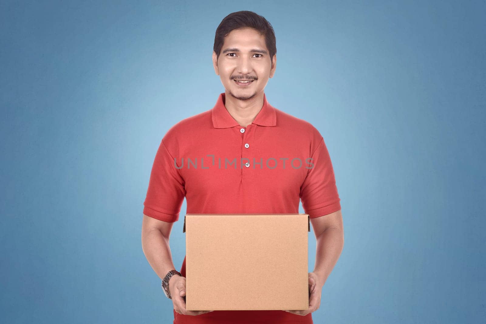 Attractive asian courier man holding package over bright background