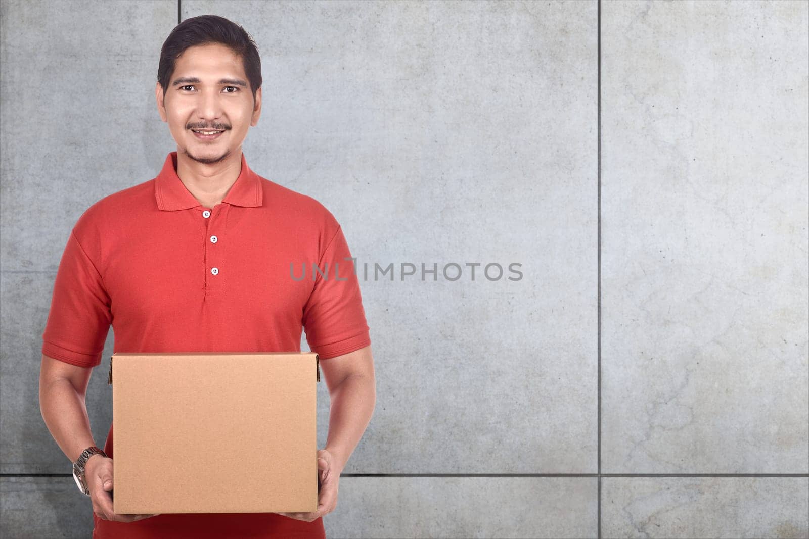 Young asian delivery man holding cardboard boxes over gray wall background
