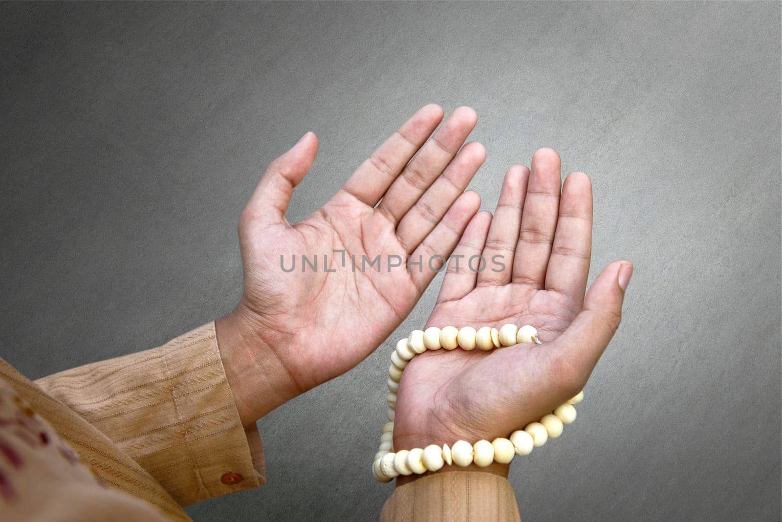 Muslim man praying with prayer beads over gray background