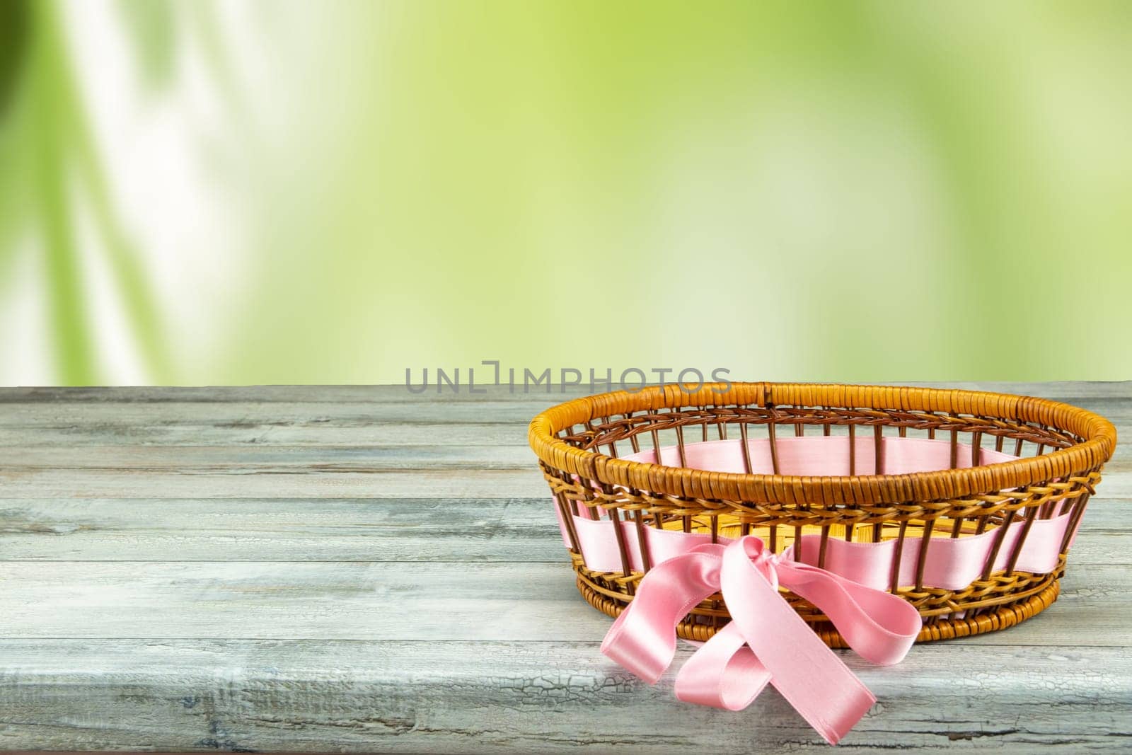 Empty basket with purple ribbon on rustic wooden table with bright green natural background. For your food and product display montage.