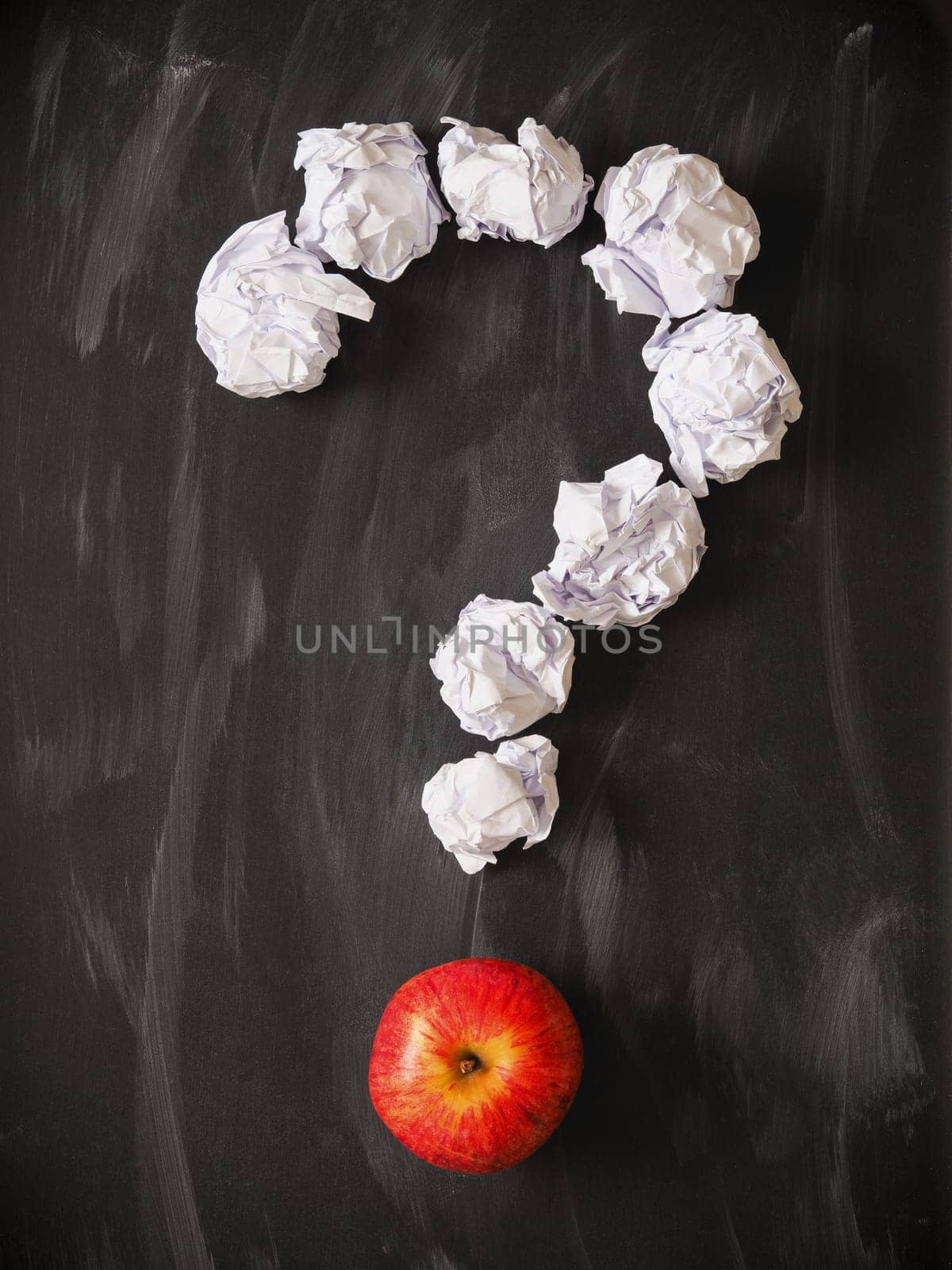 Question mark of crumpled paper with a red apple on a blackboard
