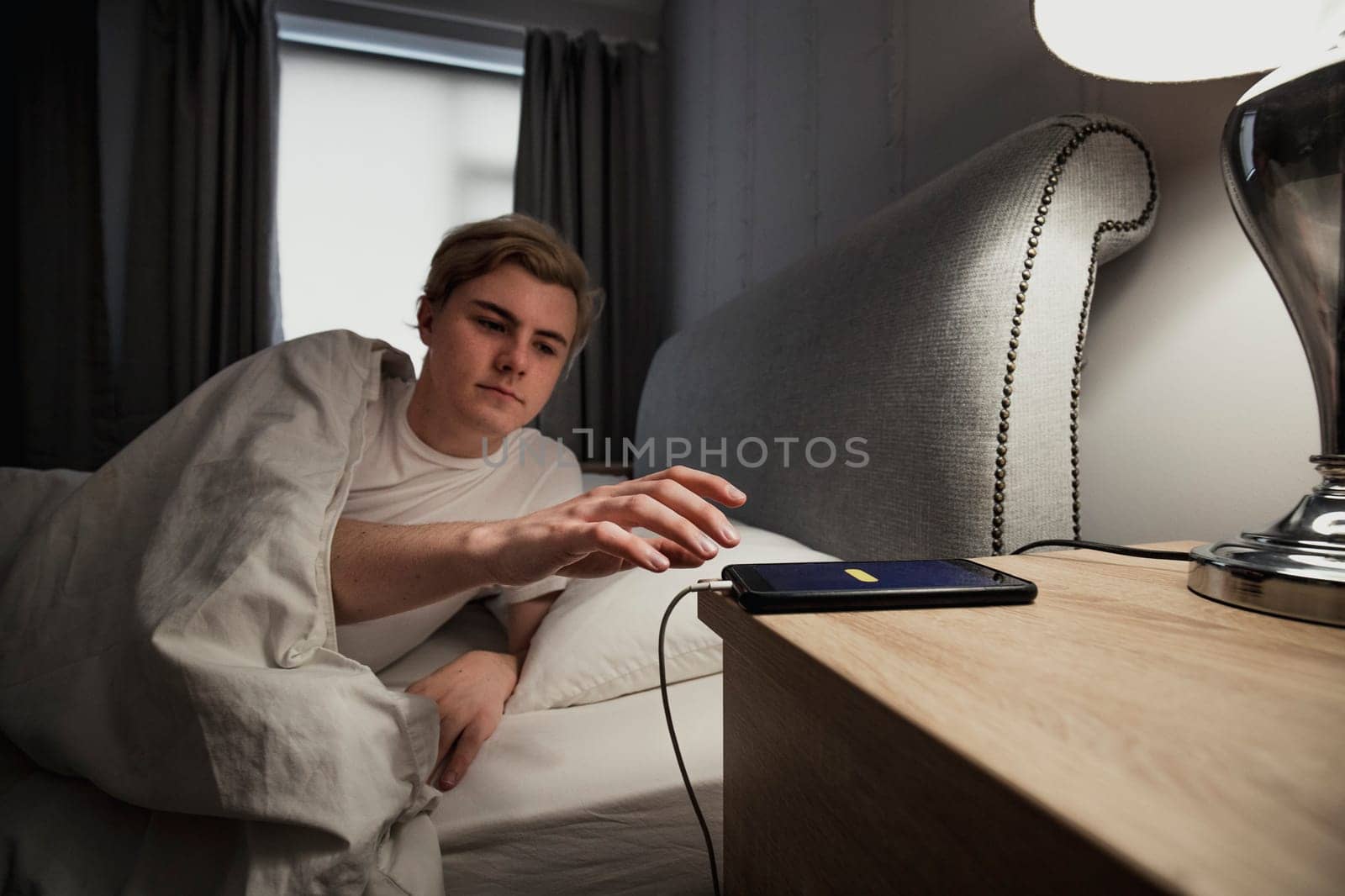 Young male adult waking up on the morning and going to turn off his alarm on his smart phone.