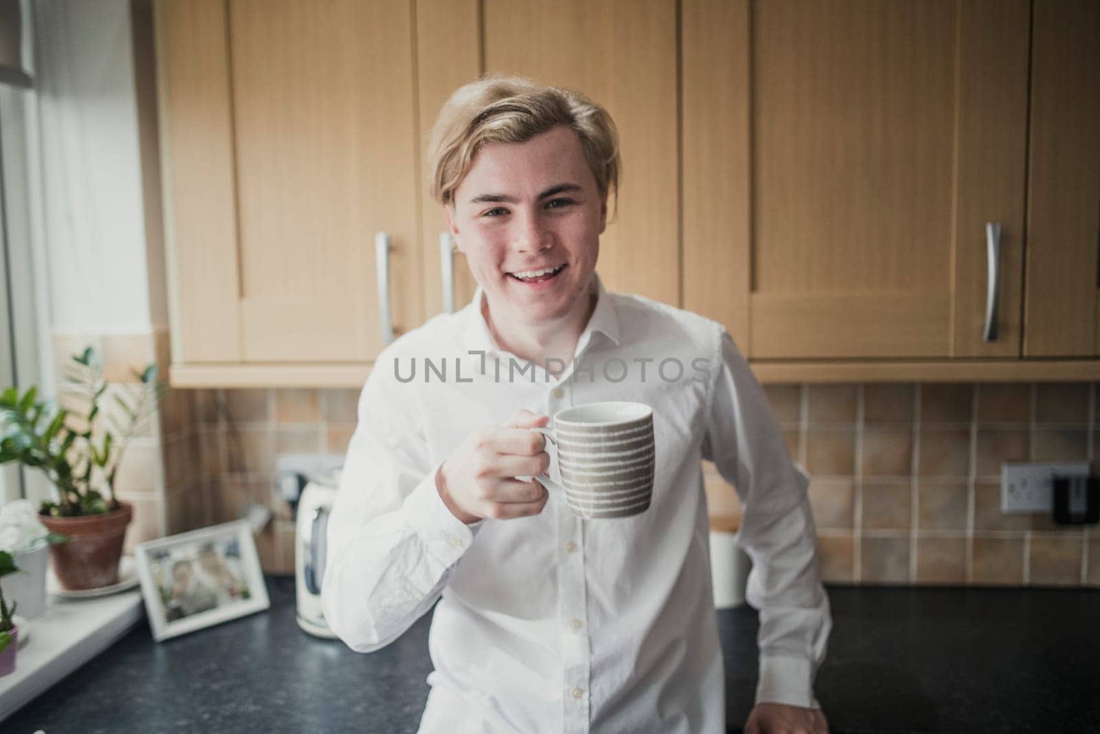 Front view of a young adult male standing in a kitchen looking at the camera with a cup of coffee.