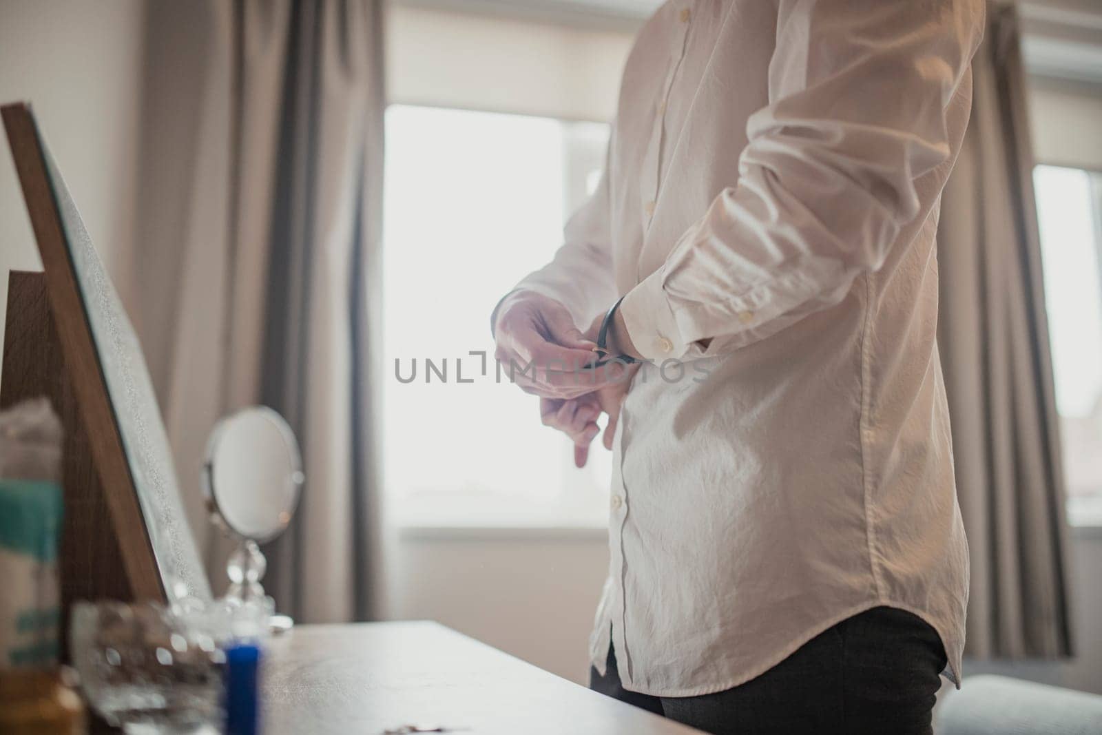 Side view of an unrecognisable person standing at a dresser table putting a watch on.