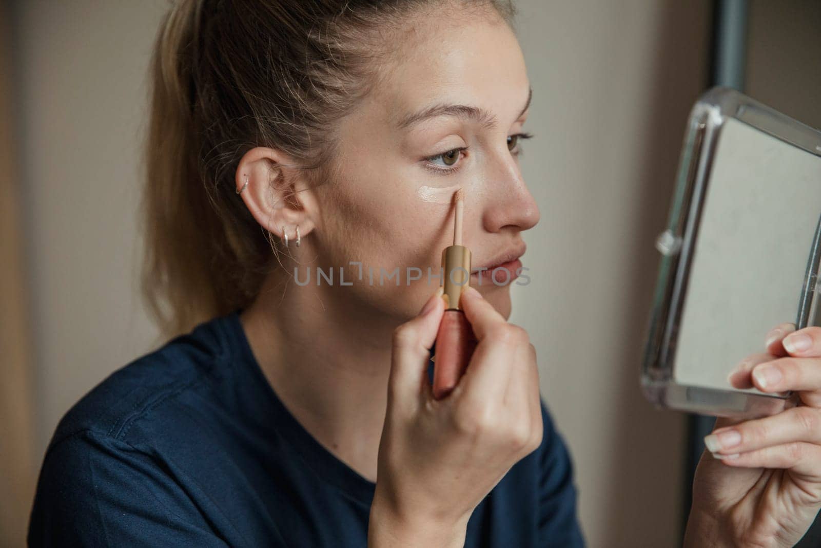 Close-up, side view of a young female adult applying make-up.