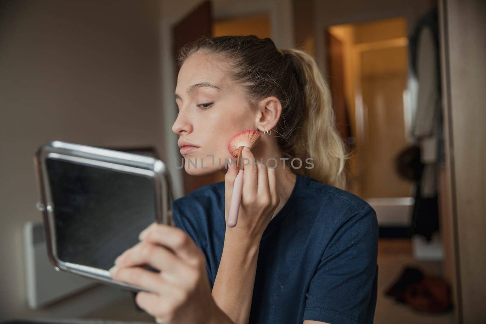 Front view of a young female adult holding a mirror while applying her make-up during her morning routine.