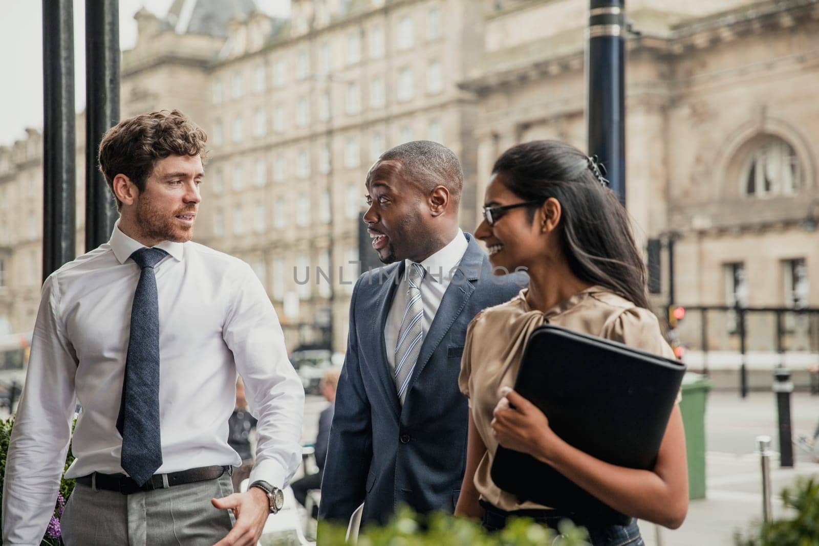 Side view of three business people walking towards the front of a hotel for a business meeting.