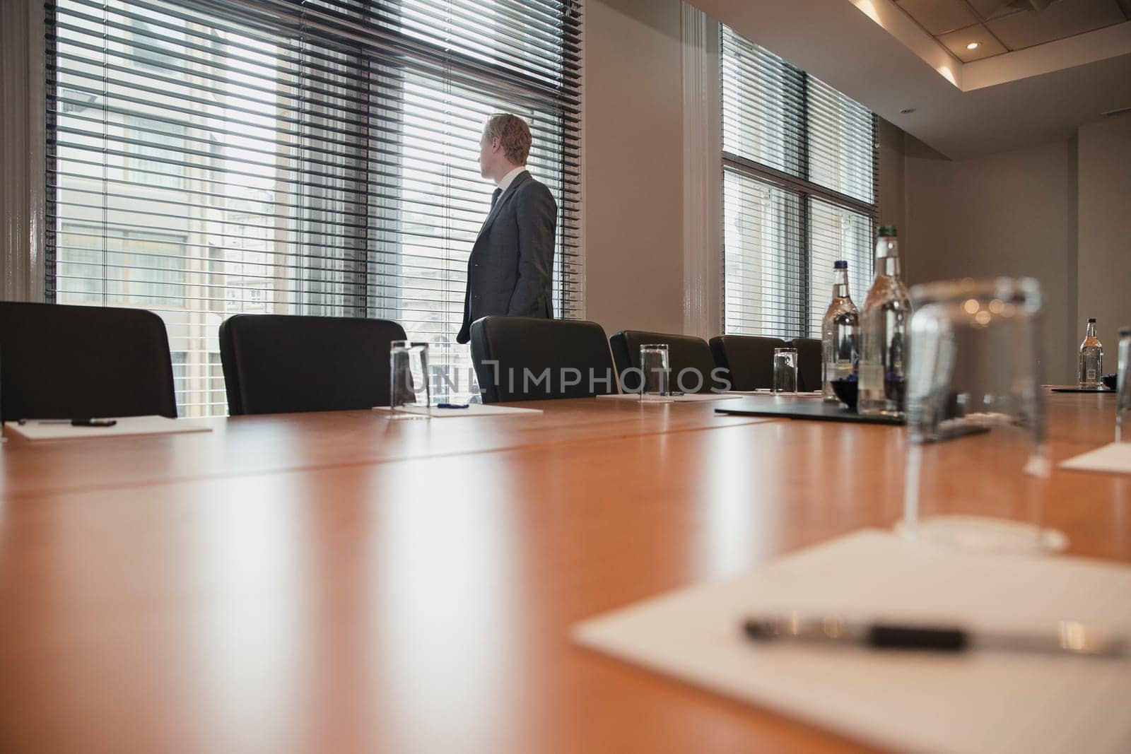 Young businessman waiting to have a meeting. Stood, looking out the window in the conference room.