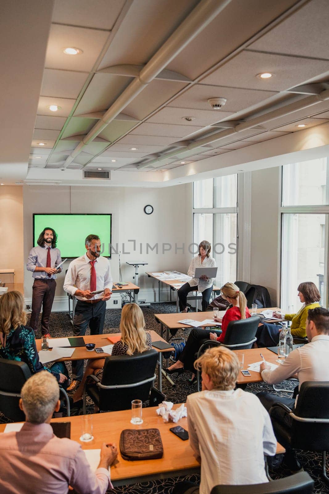 Mature male adult businessman giving a presentation at the front of the room while everyone is sat and listening.