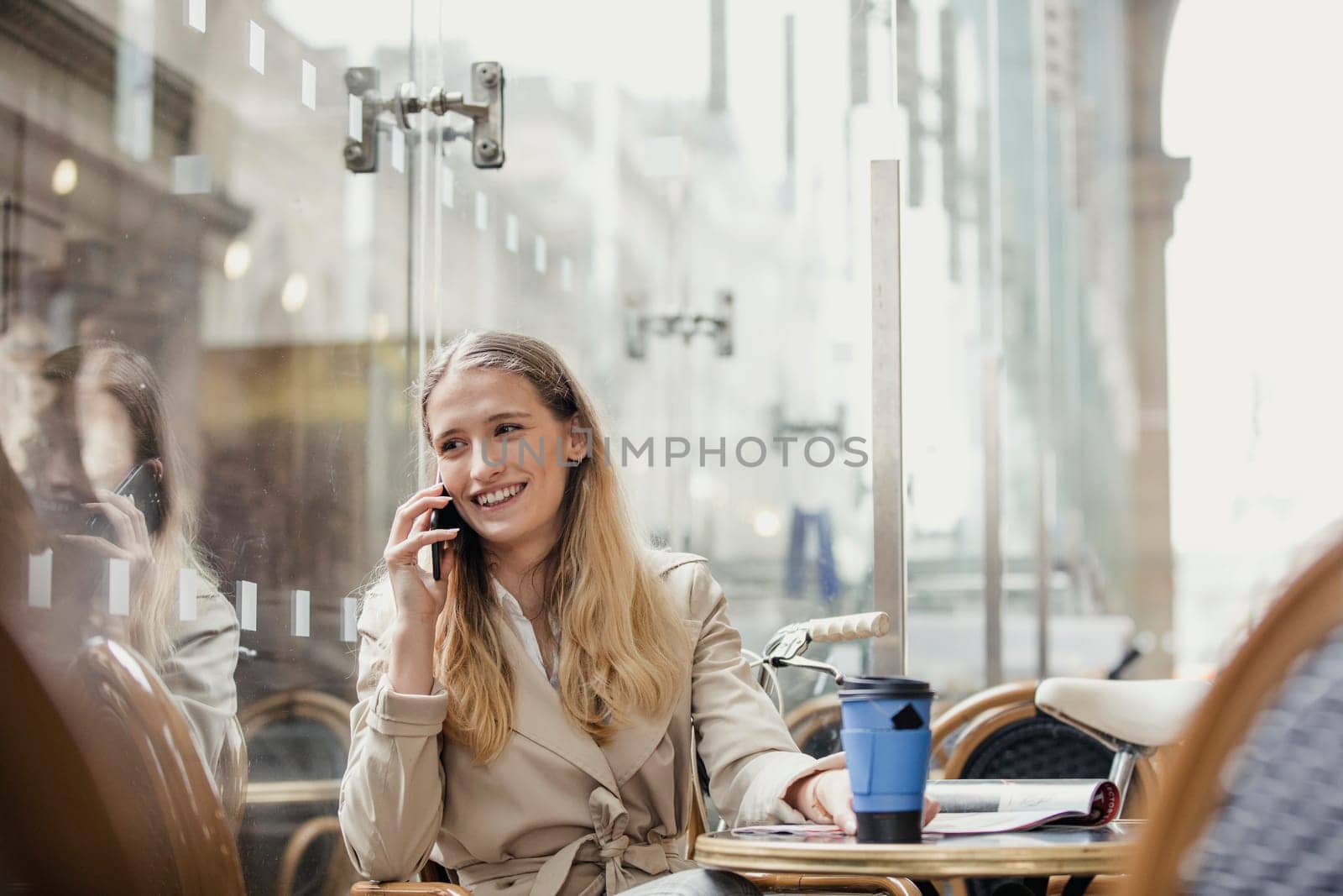 Front View of a young adult businesswoman making a phone call and having a coffee before work.