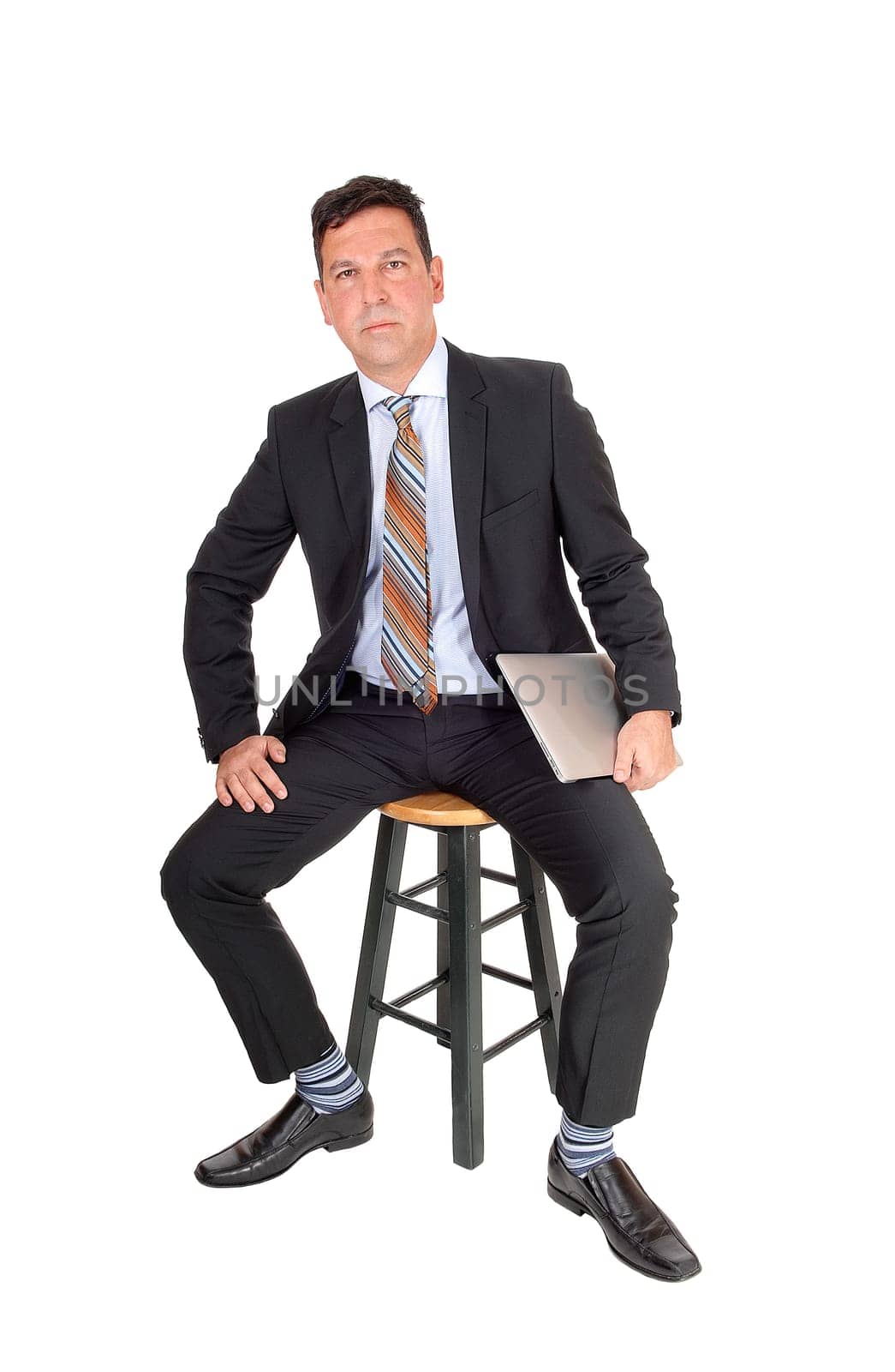 A middle age businessman sitting in a dark suit on a chair holding his.laptop in his hand, isolated for white background.